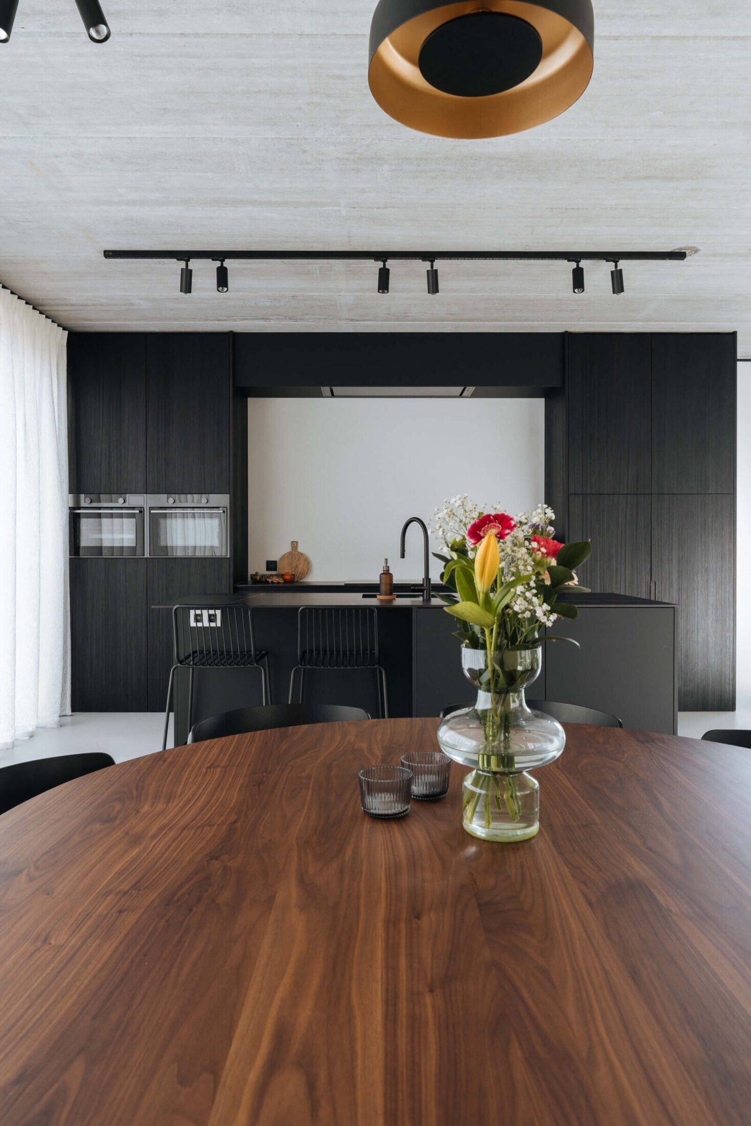 Industriële keuken in donker hout met houten eettafel en zwarte railspots in Kortrijk, Kaster Keukens
