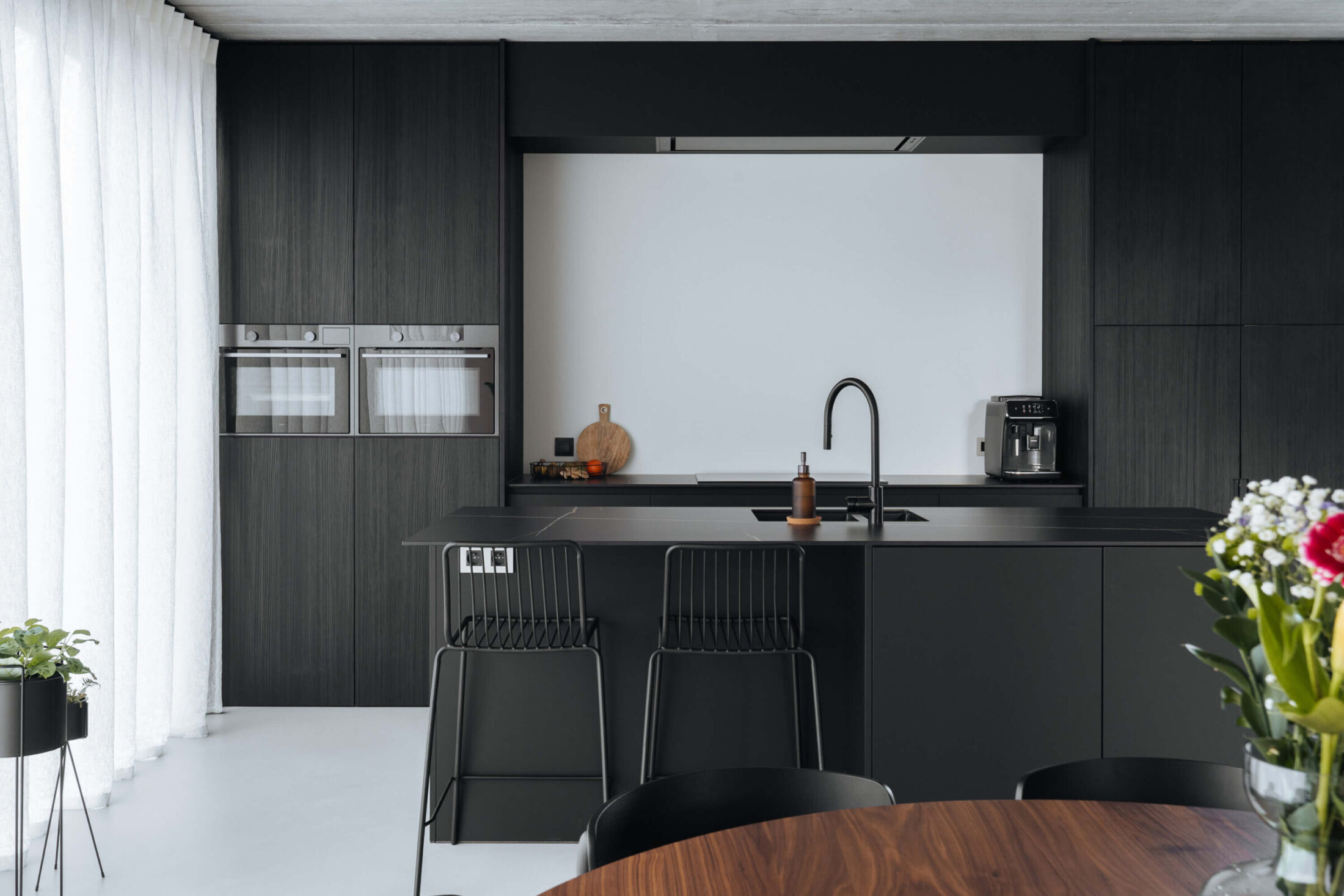 Industriële keuken met donkere houten kastenwand, zwart eiland en zwarte barkrukken in Kortrijk, Kaster Keukens