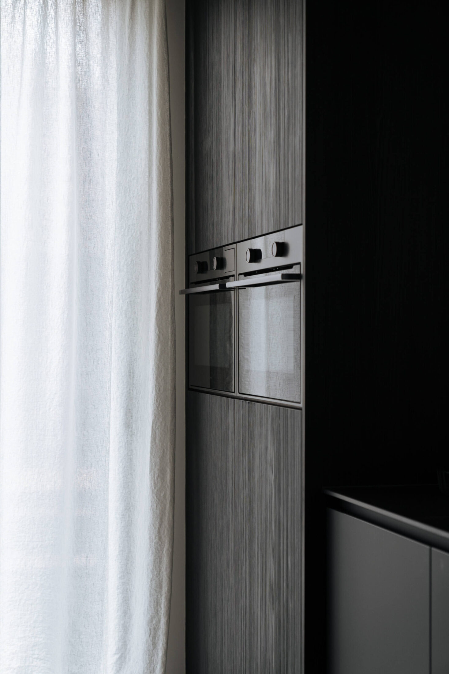 Detail van een industriële keuken met donkere houten kolomkast en ingebouwde oven in Kortrijk, Kaster Keukens