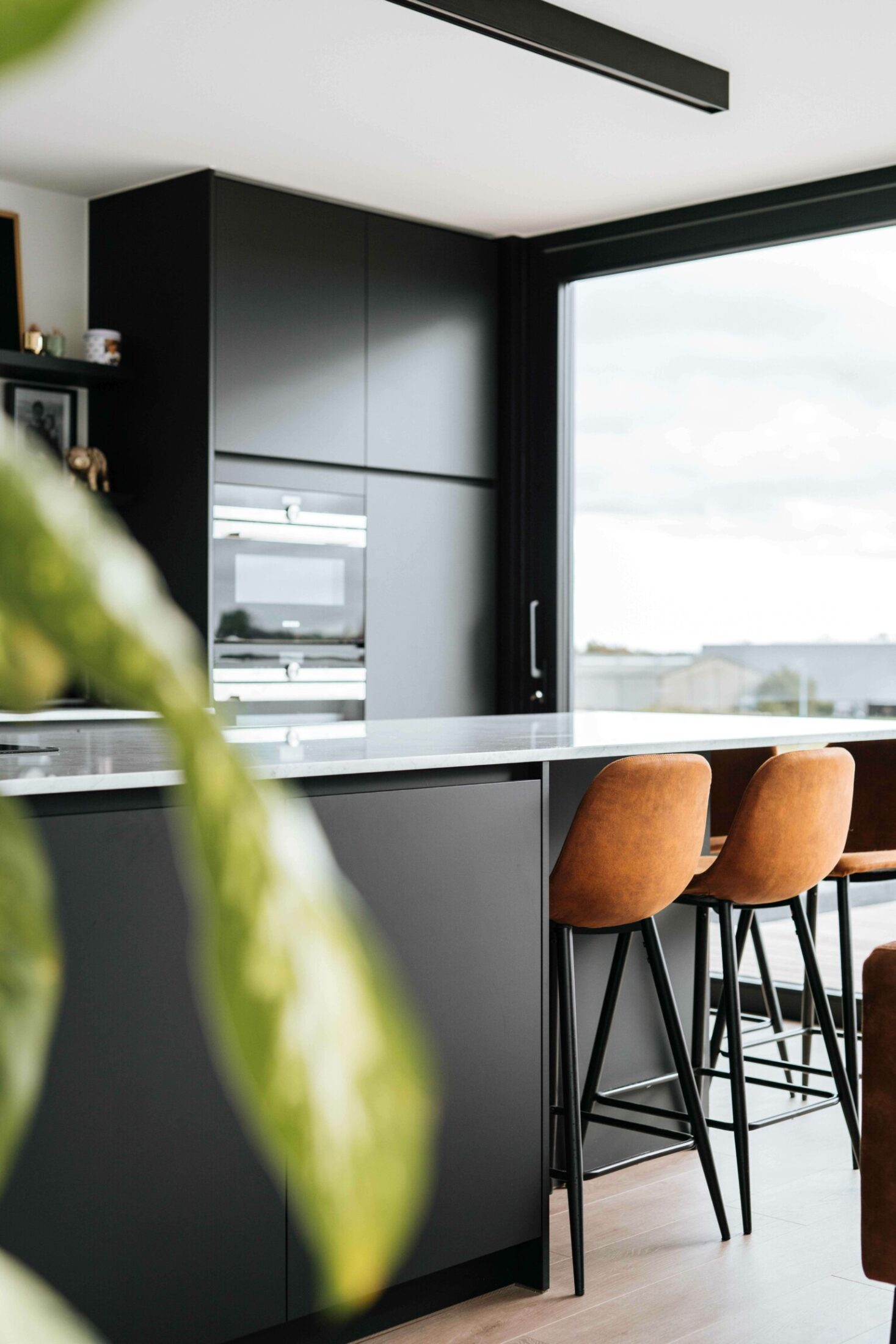 Detail van een industriële keuken met cognac barkrukken aan een zwart eiland en ovens in Roeselare, Kaster Keukens
