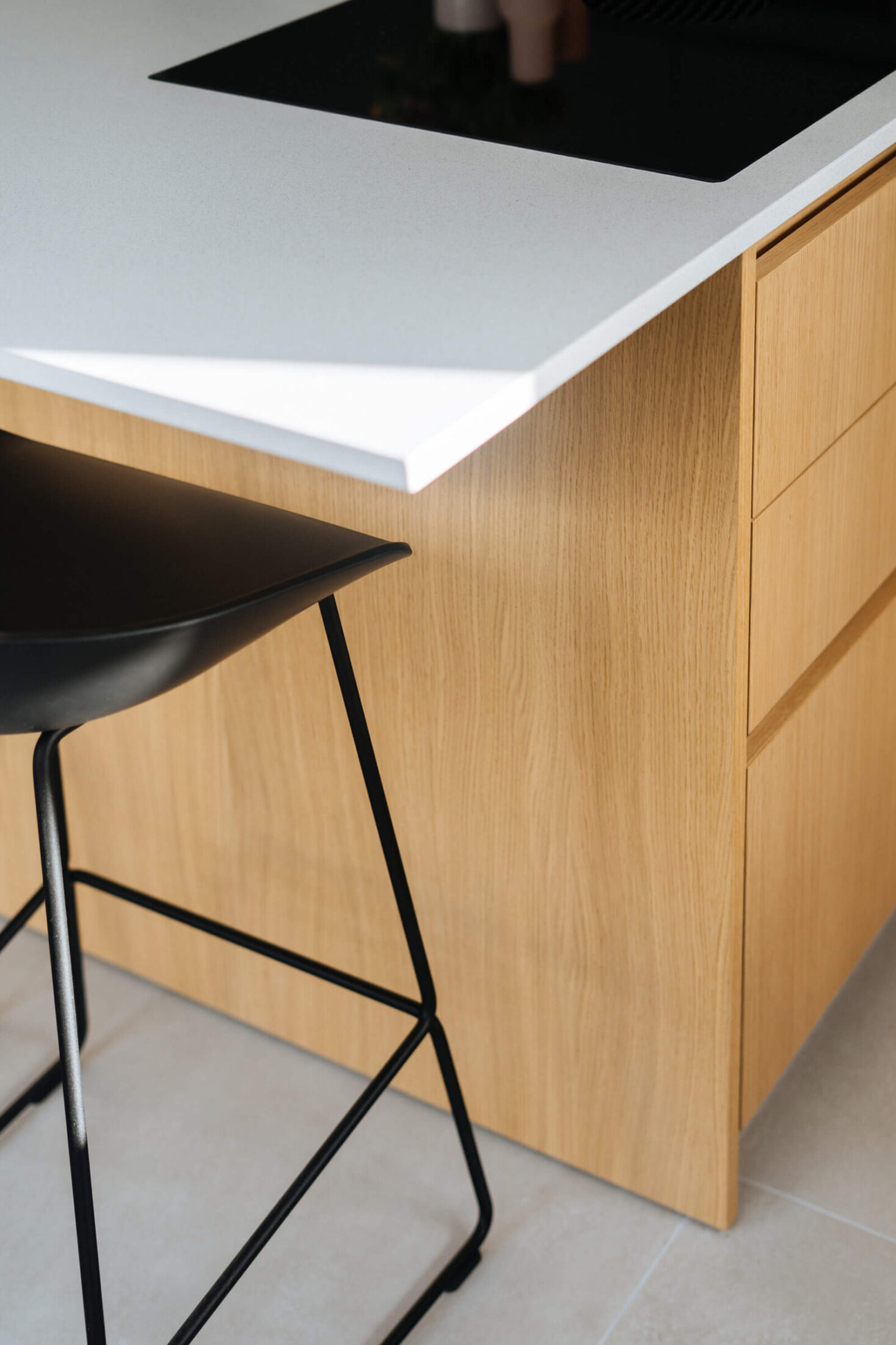 Detail van een landelijke keuken met eiken eiland, wit werkblad en zwarte barkruk in Aalter, Kaster Keukens