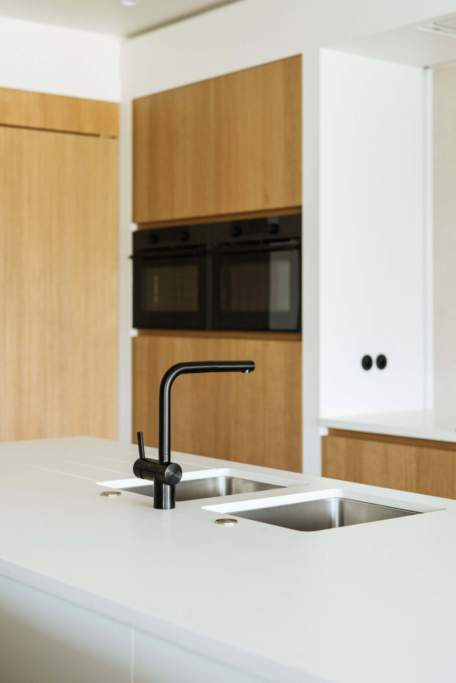 Detail van een landelijke keuken met zwarte kraan, wit werkblad en eiken ovenkast in De Haan, Kaster Keukens
