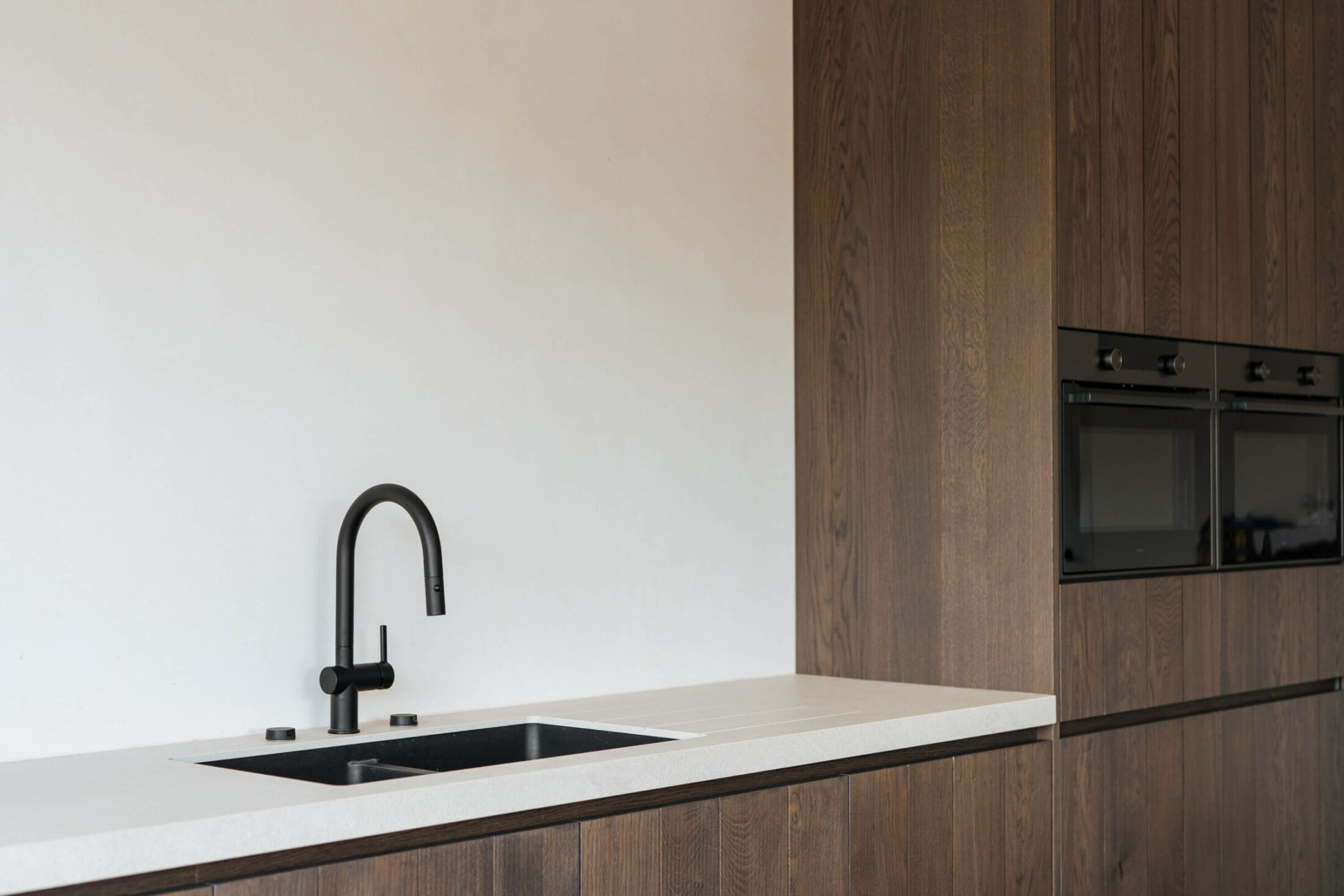 Detail van een landelijke keuken met zwarte spoelbak en hoge kast met twee ovens in Oostnieuwkerke, Kaster Keukens