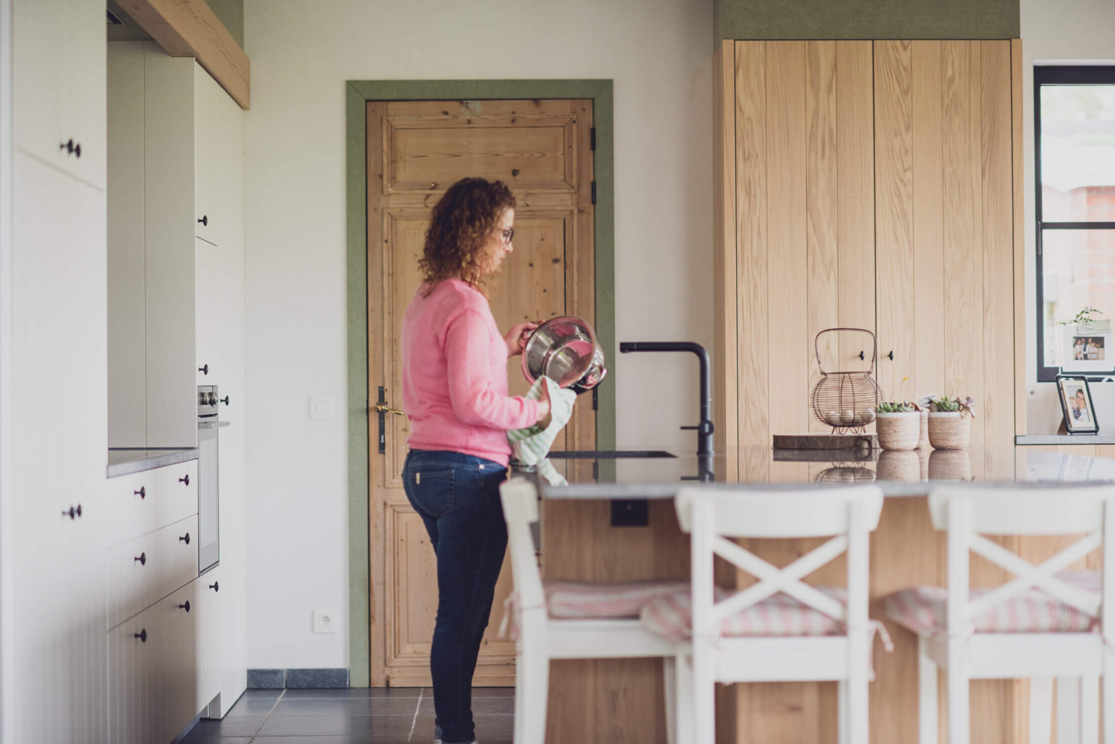 Landelijke keuken met eiken kastenwand, witte kasten en eiland met witte stoelen in Passendale, Kaster Keukens