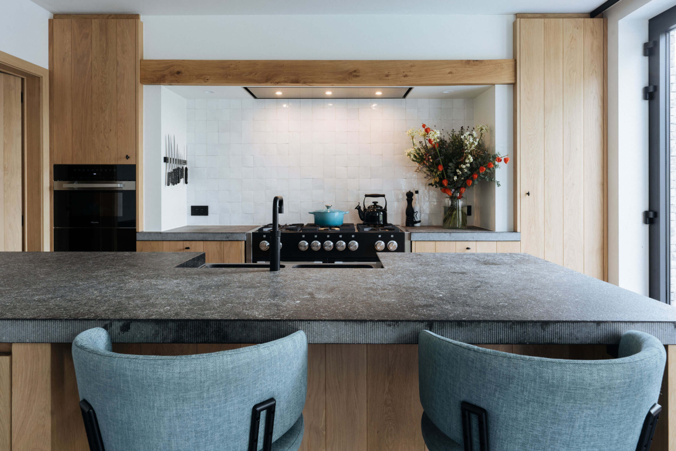 Landelijke keuken met eiken kastenwand, zwart fornuis en natuursteen eiland in Roeselare, Kaster Keukens