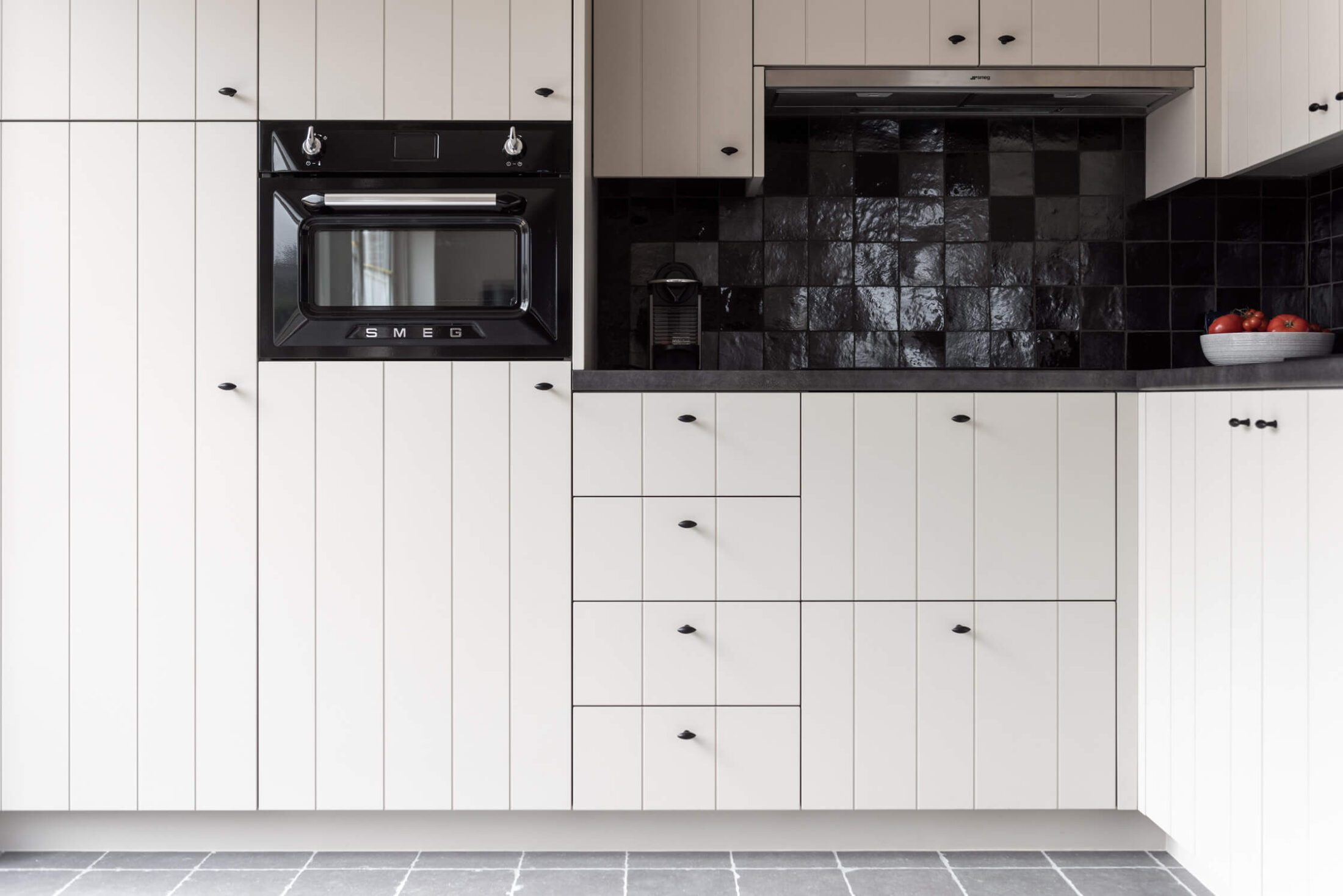Landelijke keuken met witte kastenwand met groeven, compacte oven en zwarte tegels in Roeselare, Kaster Keukens
