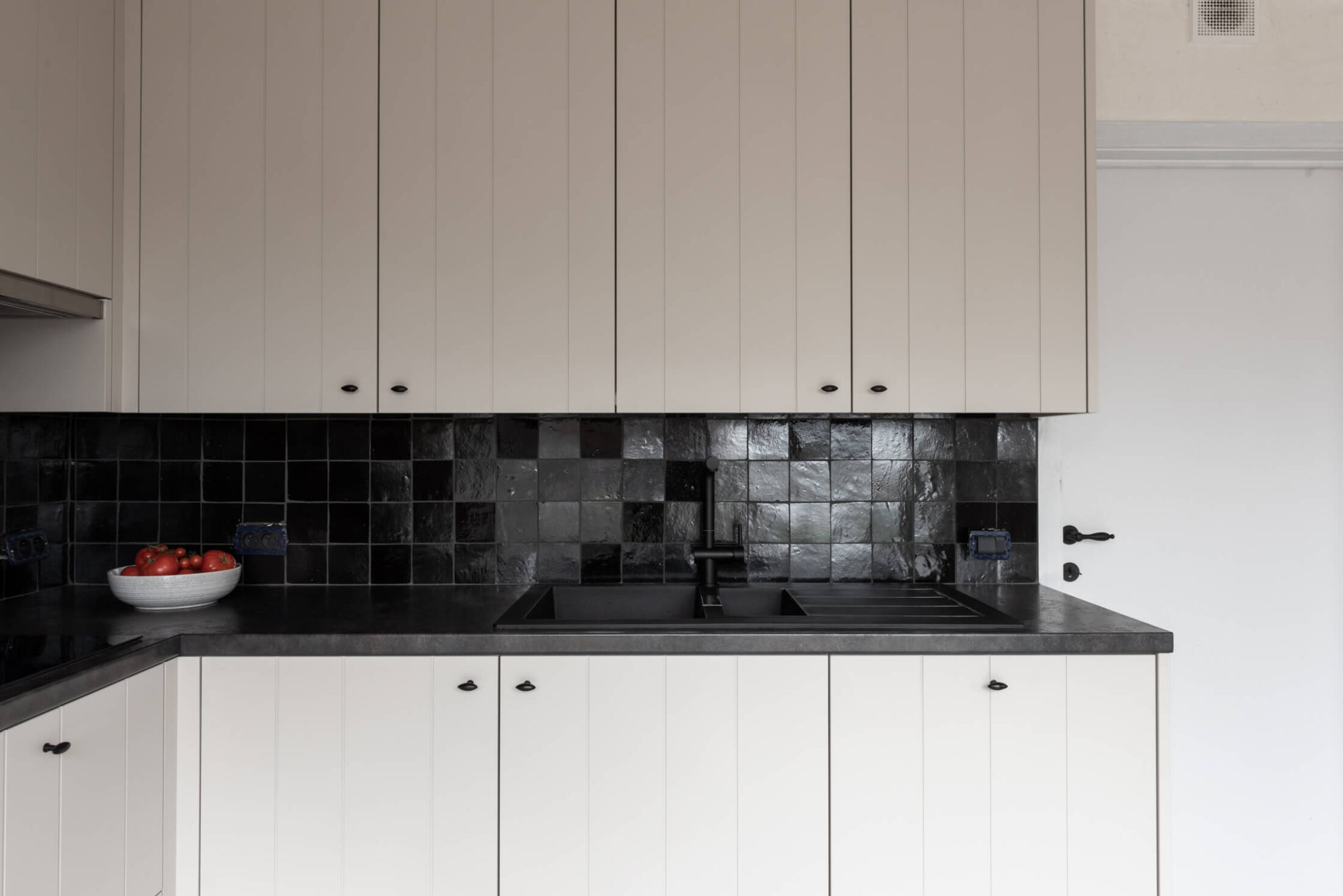 Landelijke keuken in hoekopstelling met witte fronten, donker werkblad en zwarte wandtegels in Roeselare, Kaster Keukens