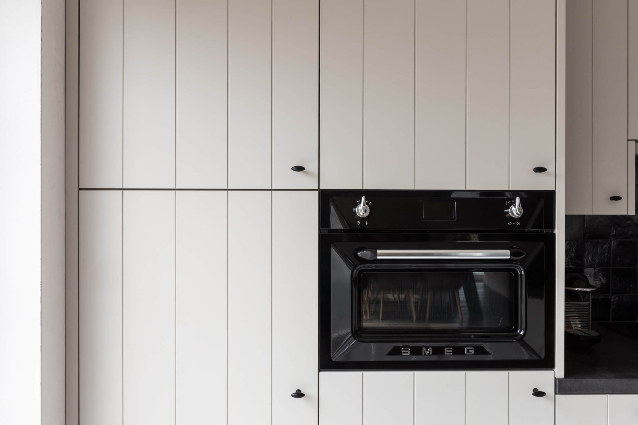 Detail van een landelijke keuken met witte kastenwand en zwarte retro oven in Roeselare, Kaster Keukens