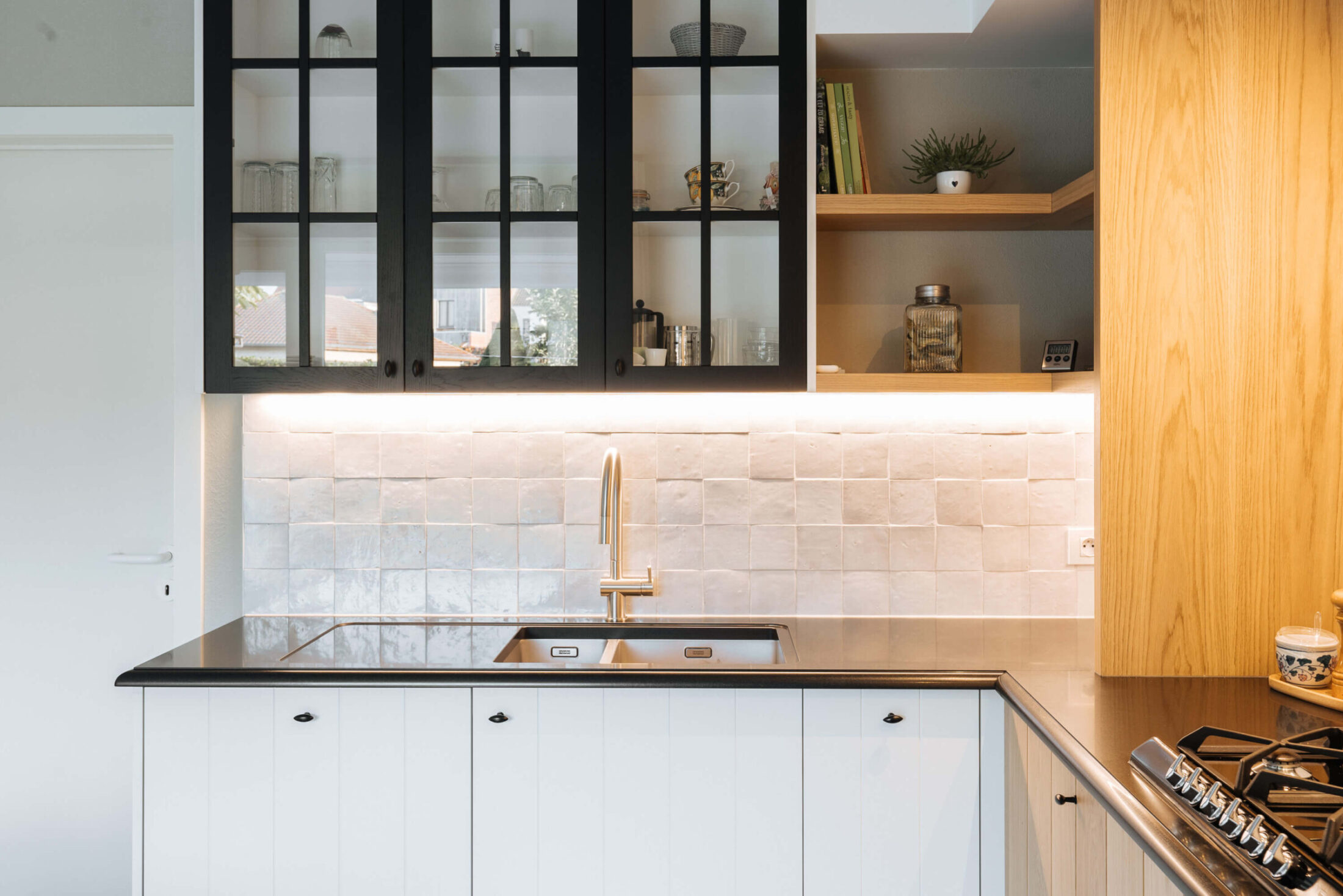 Landelijke keuken met zwarte glazen bovenkasten, witte onderkasten en zwart werkblad in Veurne, Kaster Keukens