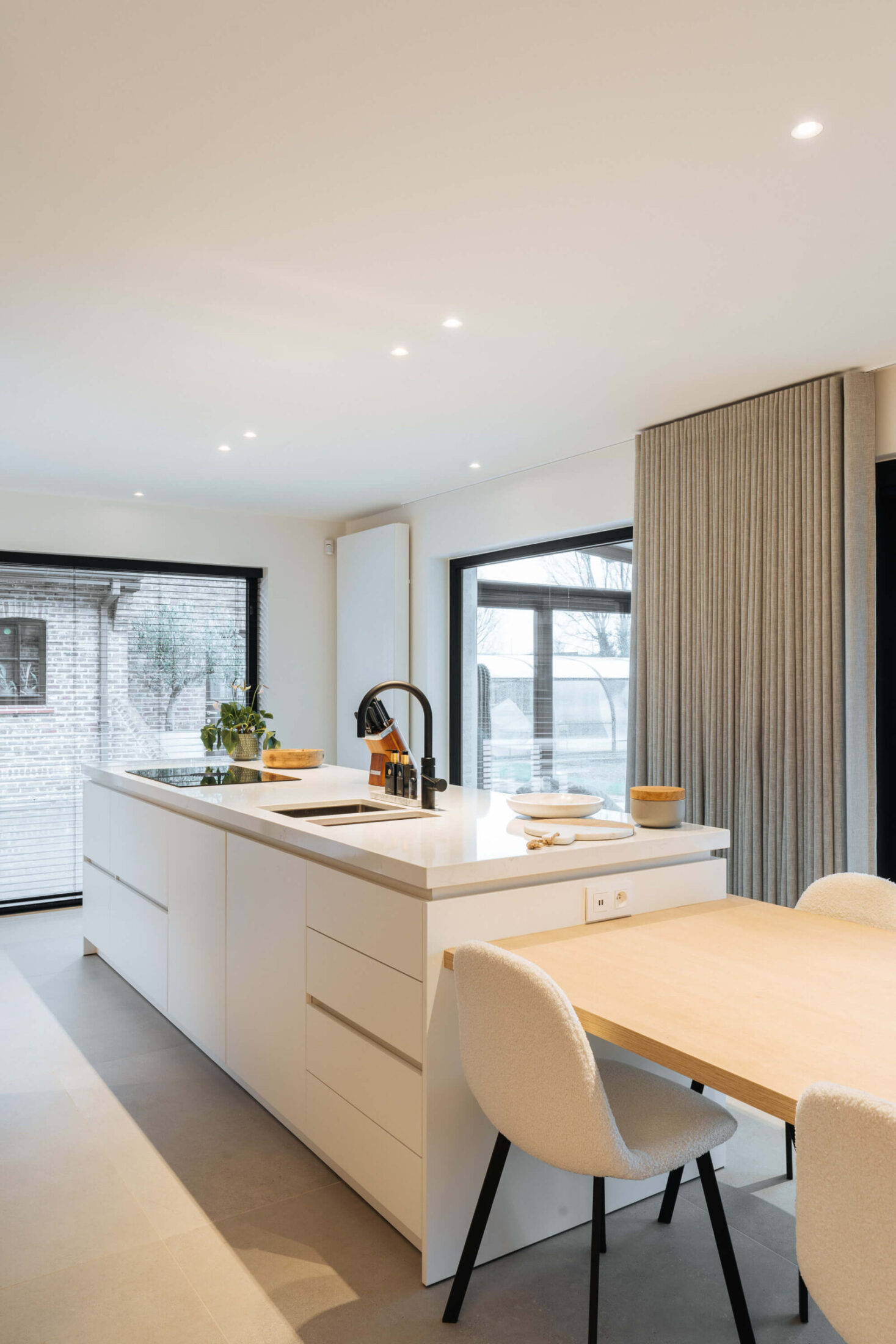 Moderne keuken met wit eiland, eiken eettafel en witte stoelen in Bellegem, Kaster Keukens