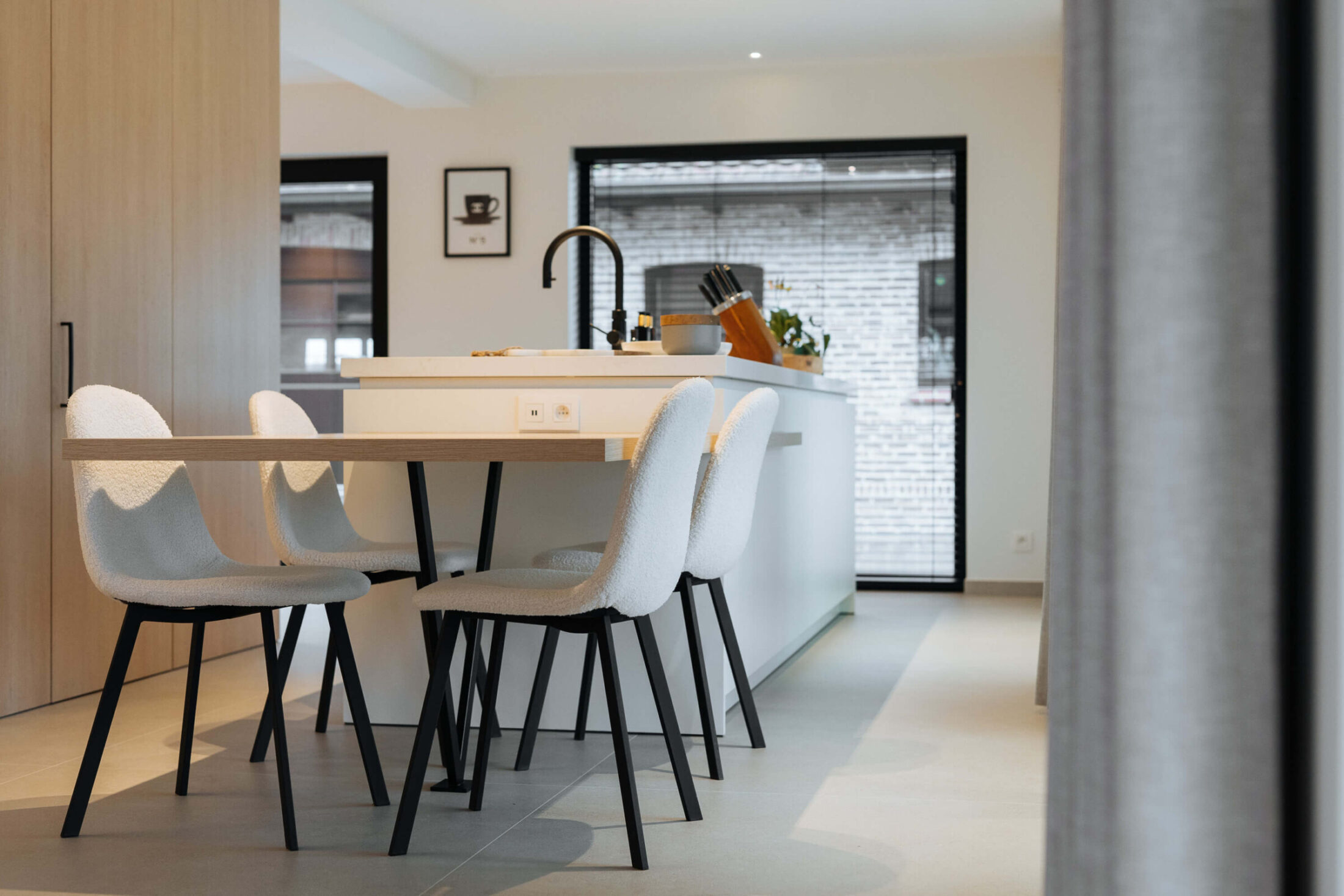 Moderne keuken met eethoek, witte stoelen en wit eiland bij de tuindeur in Bellegem, Kaster Keukens