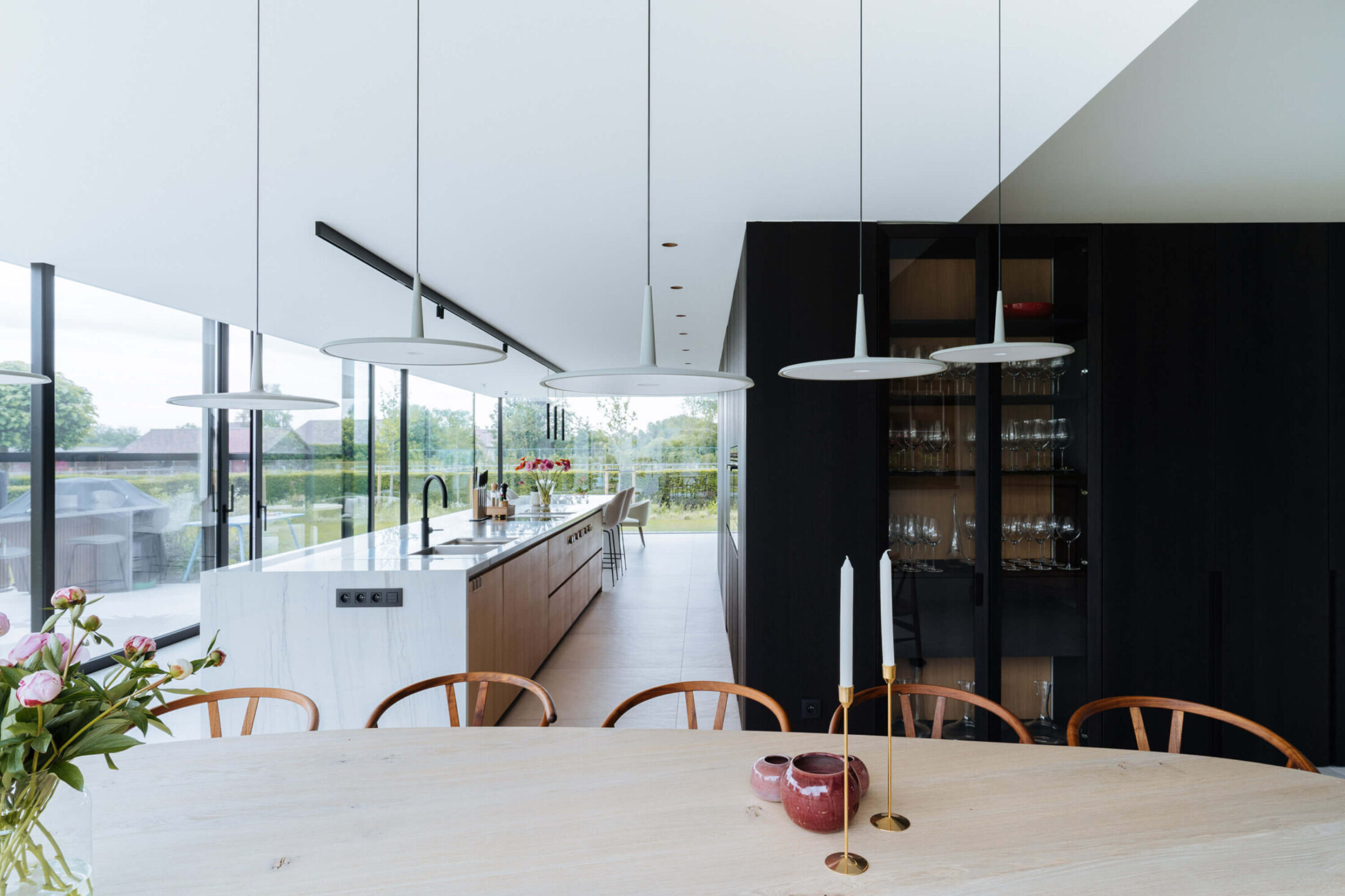 Moderne keuken met zwarte kastenwand met glazen vitrine, wit eiland en eettafel in Gent, Kaster Keukens