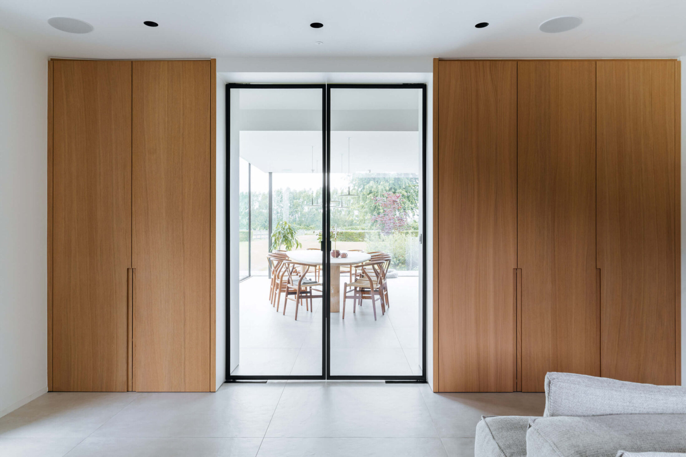 Moderne leefruimte met hoge eiken kastenwand rond een stalen deur in Gent, Kaster Keukens