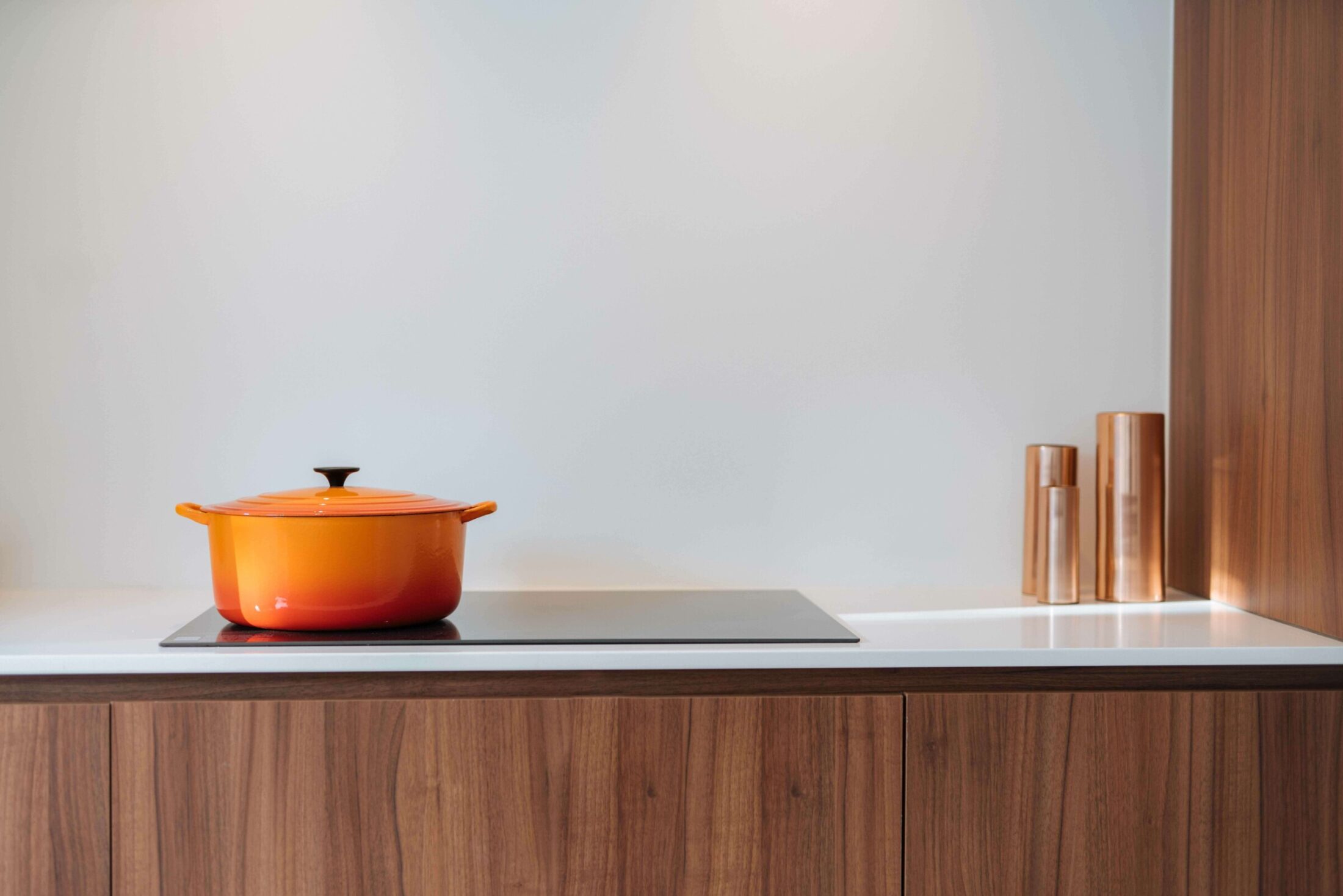 Detail van een moderne keuken met notelaar onderkasten en inductiekookplaat in Kortrijk, Kaster Keukens