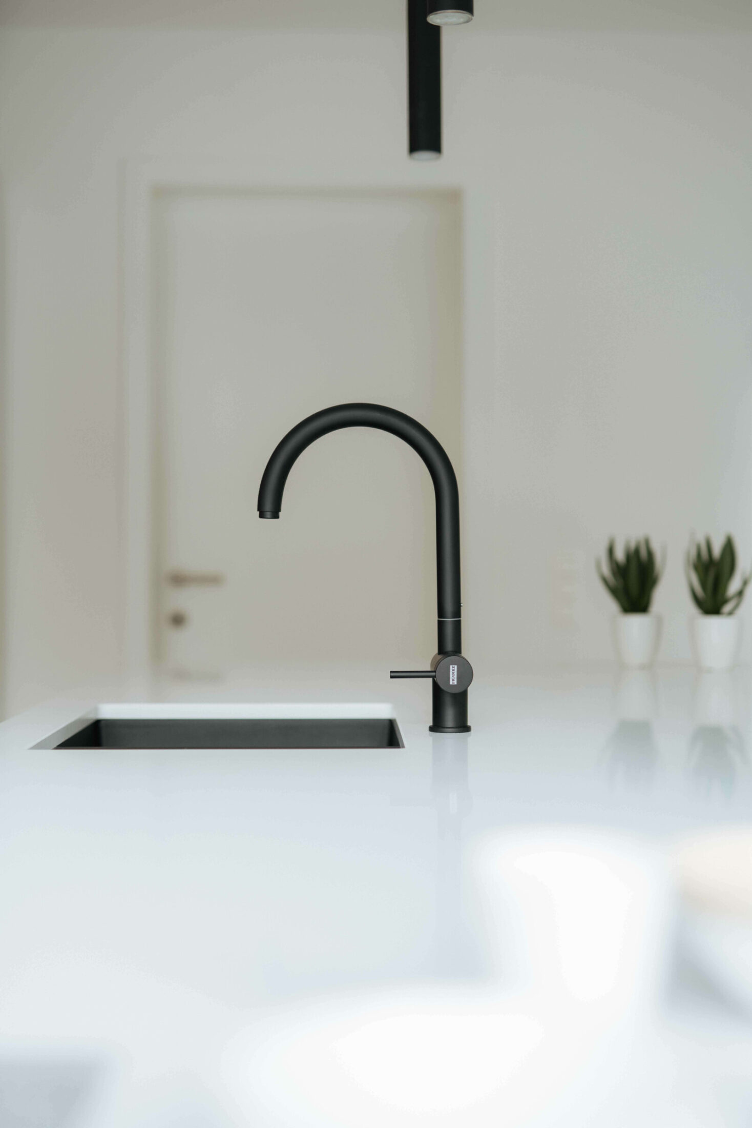 Detail van een moderne keuken met zwarte kraan en spoelbak in wit werkblad in Kortrijk, Kaster Keukens