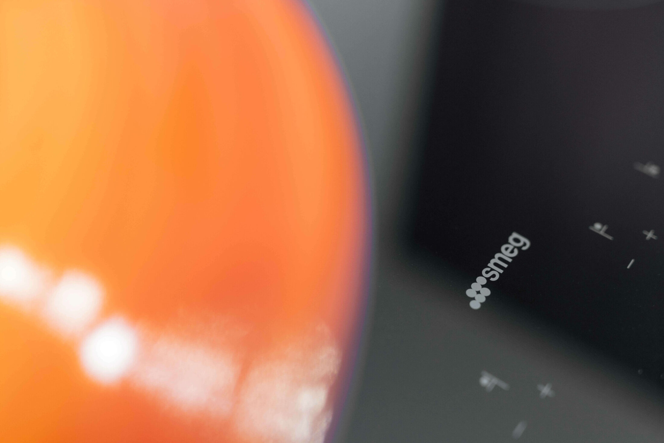 Detail van een moderne keuken met oranje kookpot op een zwarte kookplaat in Kortrijk, Kaster Keukens