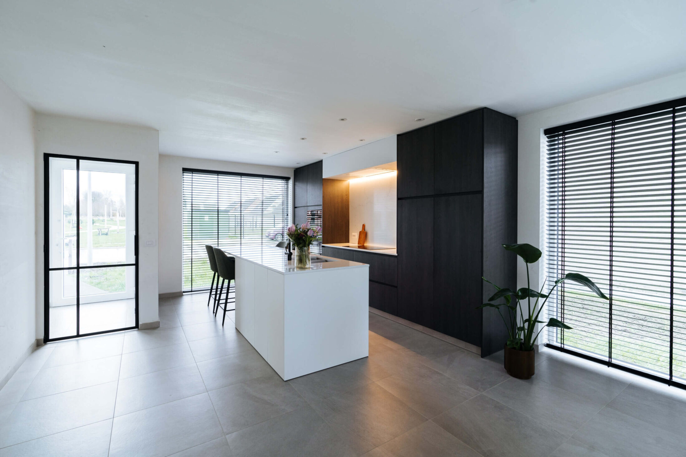 Moderne keuken met wit eiland, zwarte hoge kasten en stalen deur in Meulebeke, Kaster Keukens