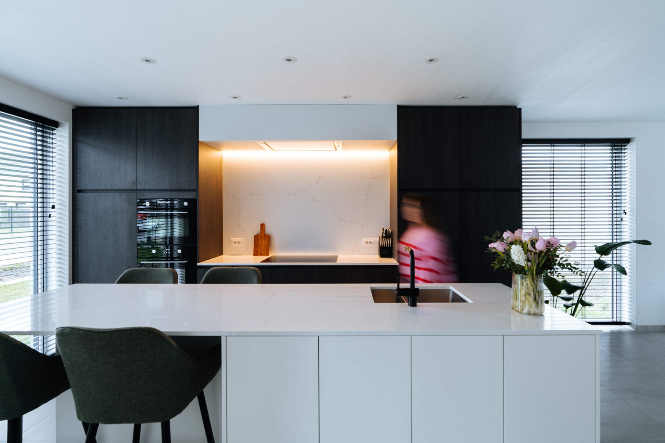 Moderne keuken met wit eiland, groene barkrukken en verlichte nis in Meulebeke, Kaster Keukens