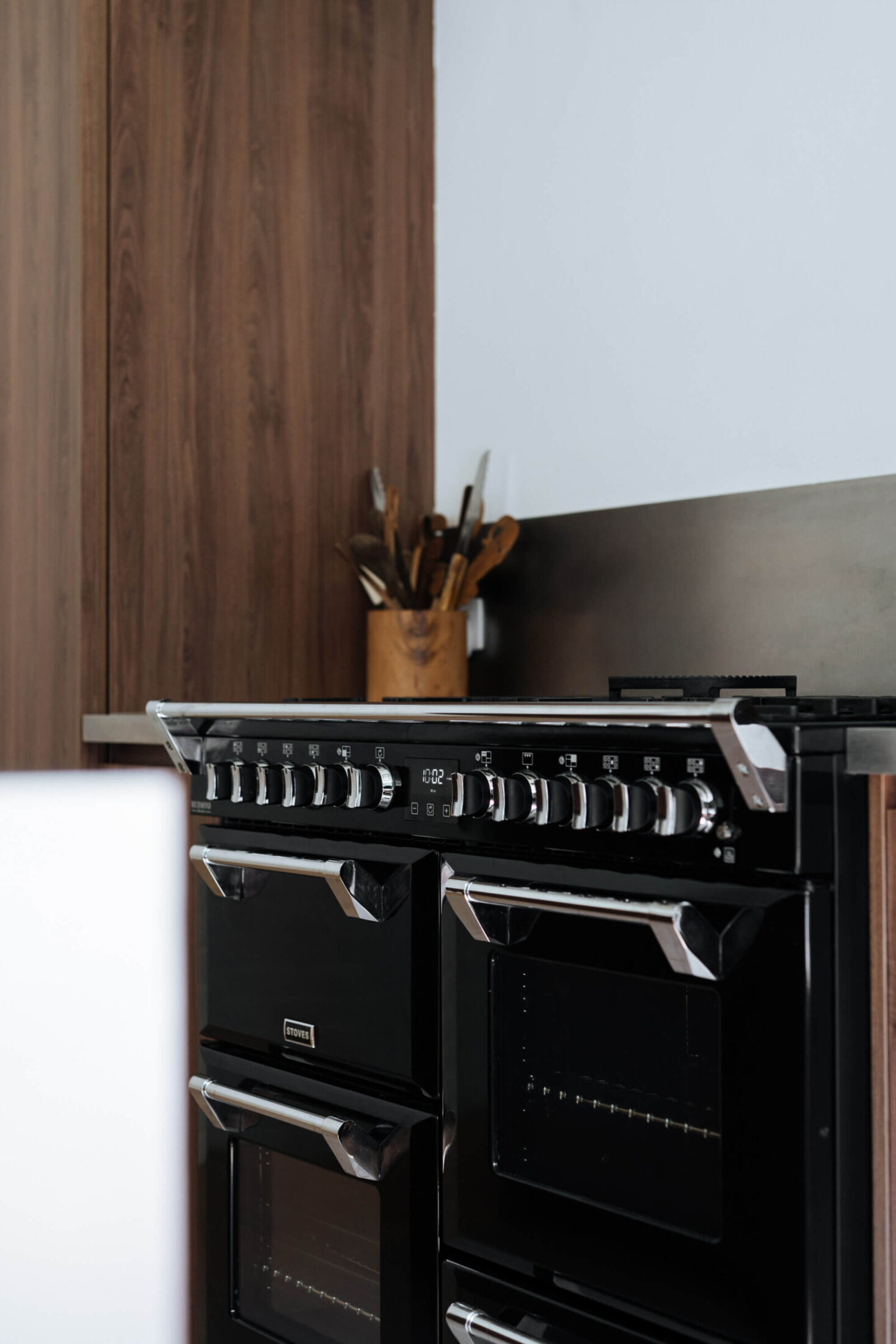 Detail van een moderne keuken met zwart fornuis tussen notelaar kasten in Mollem, Kaster Keukens