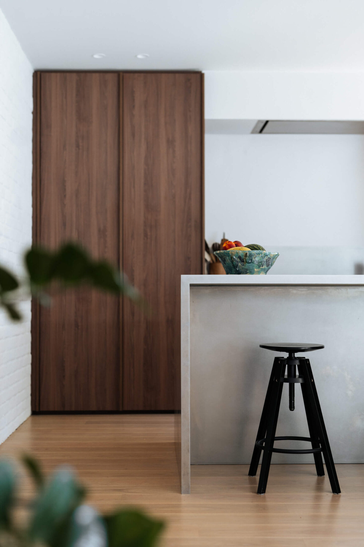 Moderne keuken met notelaar kolomkasten en zwarte kruk aan een inox werkblad in Mollem, Kaster Keukens