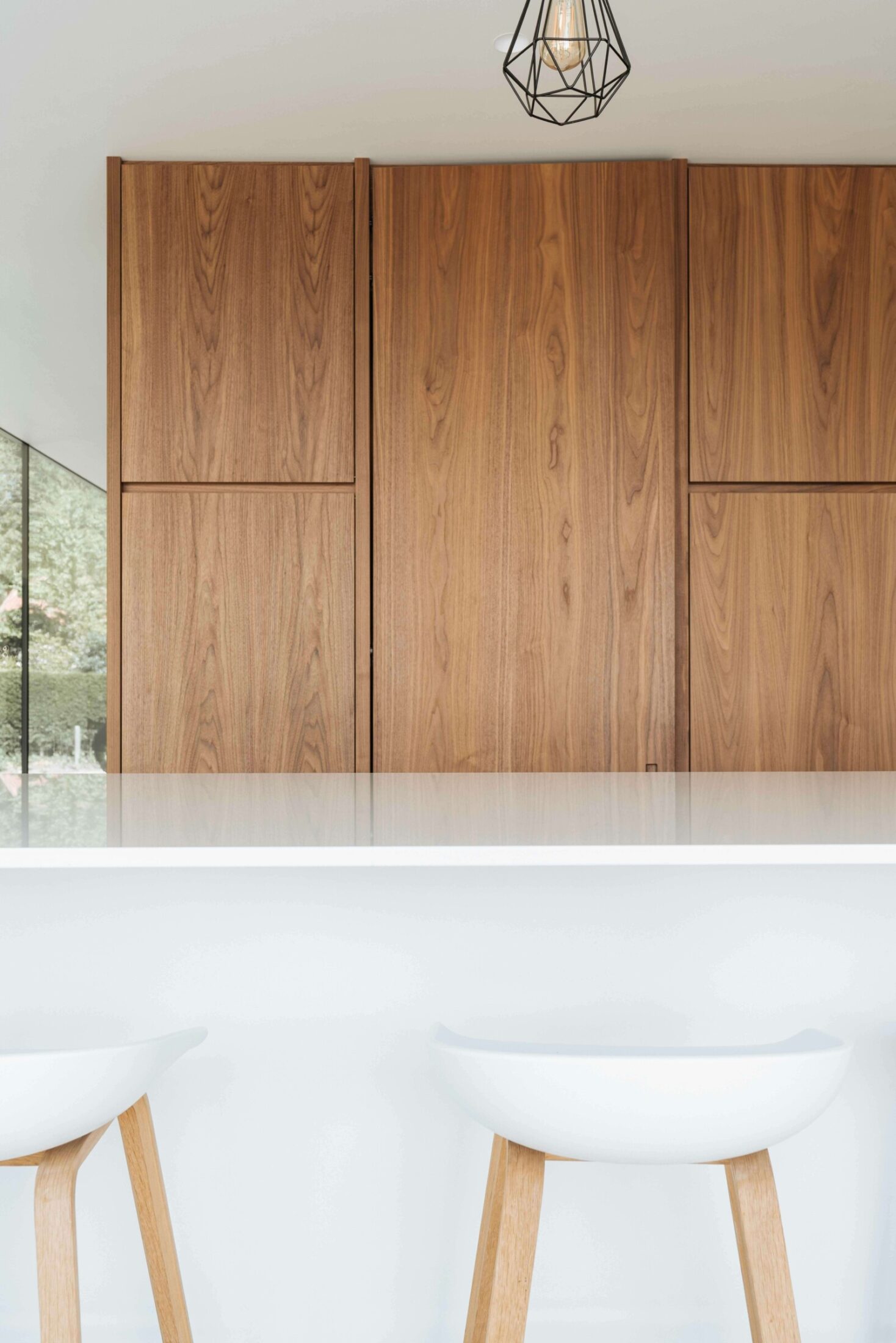 Moderne keuken met houten hoge kastenwand en witte barkrukken aan het eiland in Roeselare, Kaster Keukens
