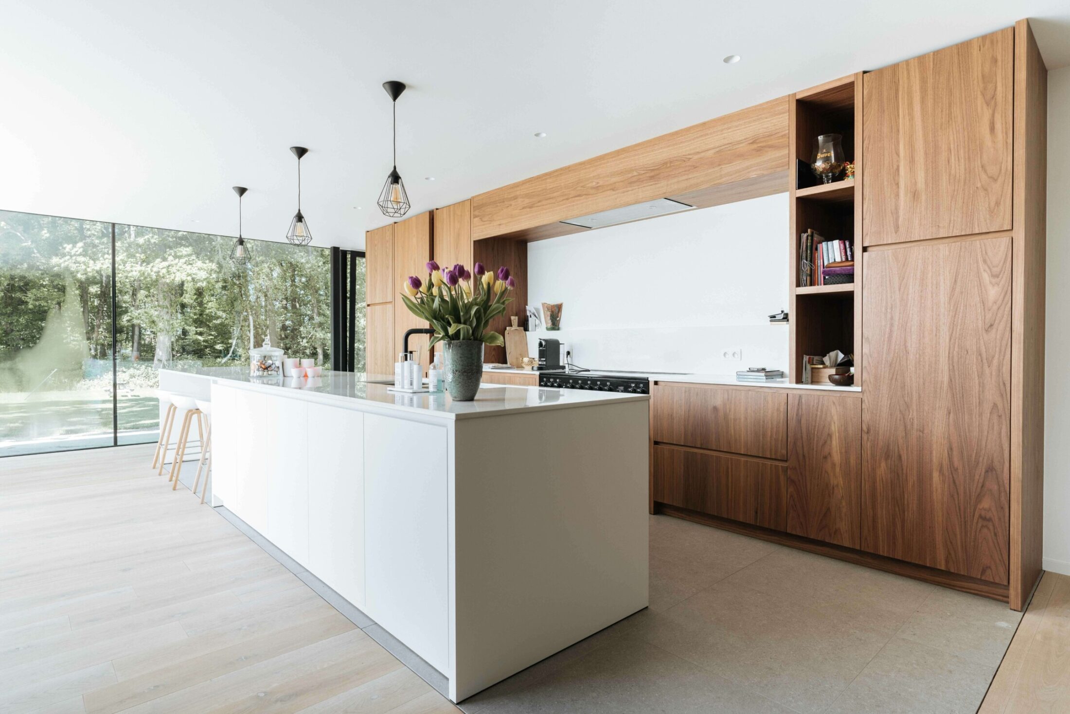 Moderne keuken met lang wit eiland, houten kastenwand en open nissen in Roeselare, Kaster Keukens