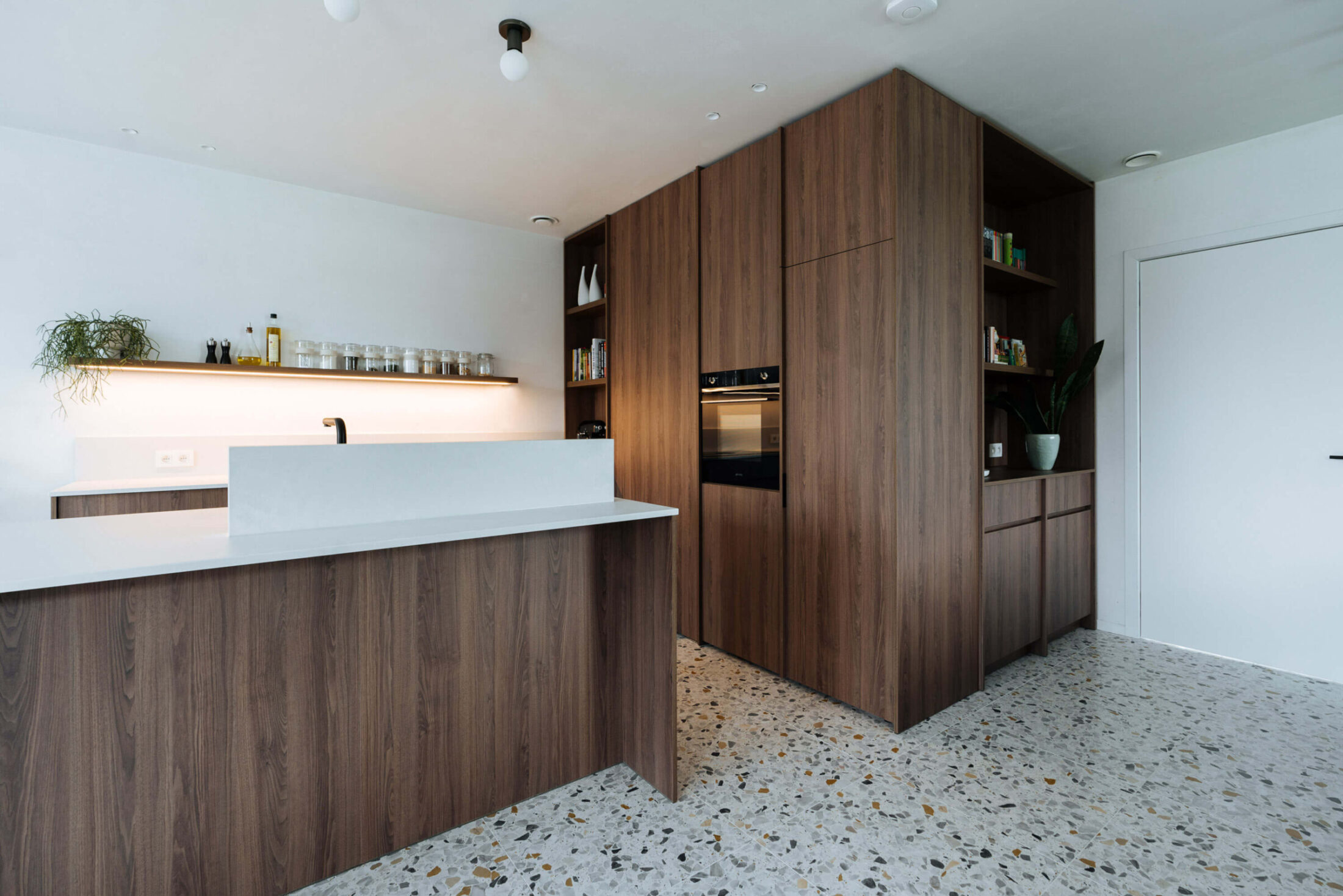 Moderne keuken met donkere houten fronten, wit werkblad en terrazzovloer in Roeselare, Kaster Keukens