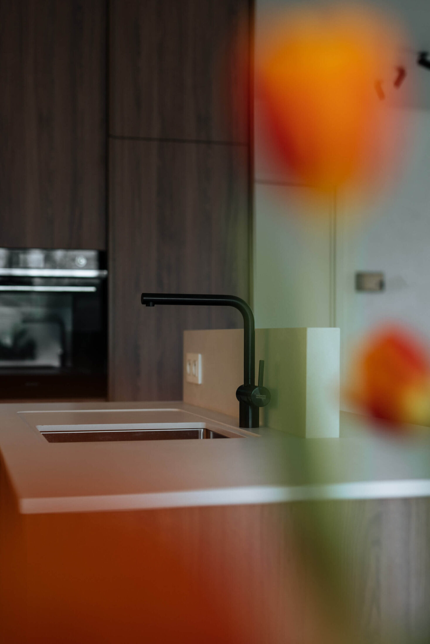 Detail van een moderne keuken met zwarte kraan en ovens in donkere houten kast in Roeselare, Kaster Keukens