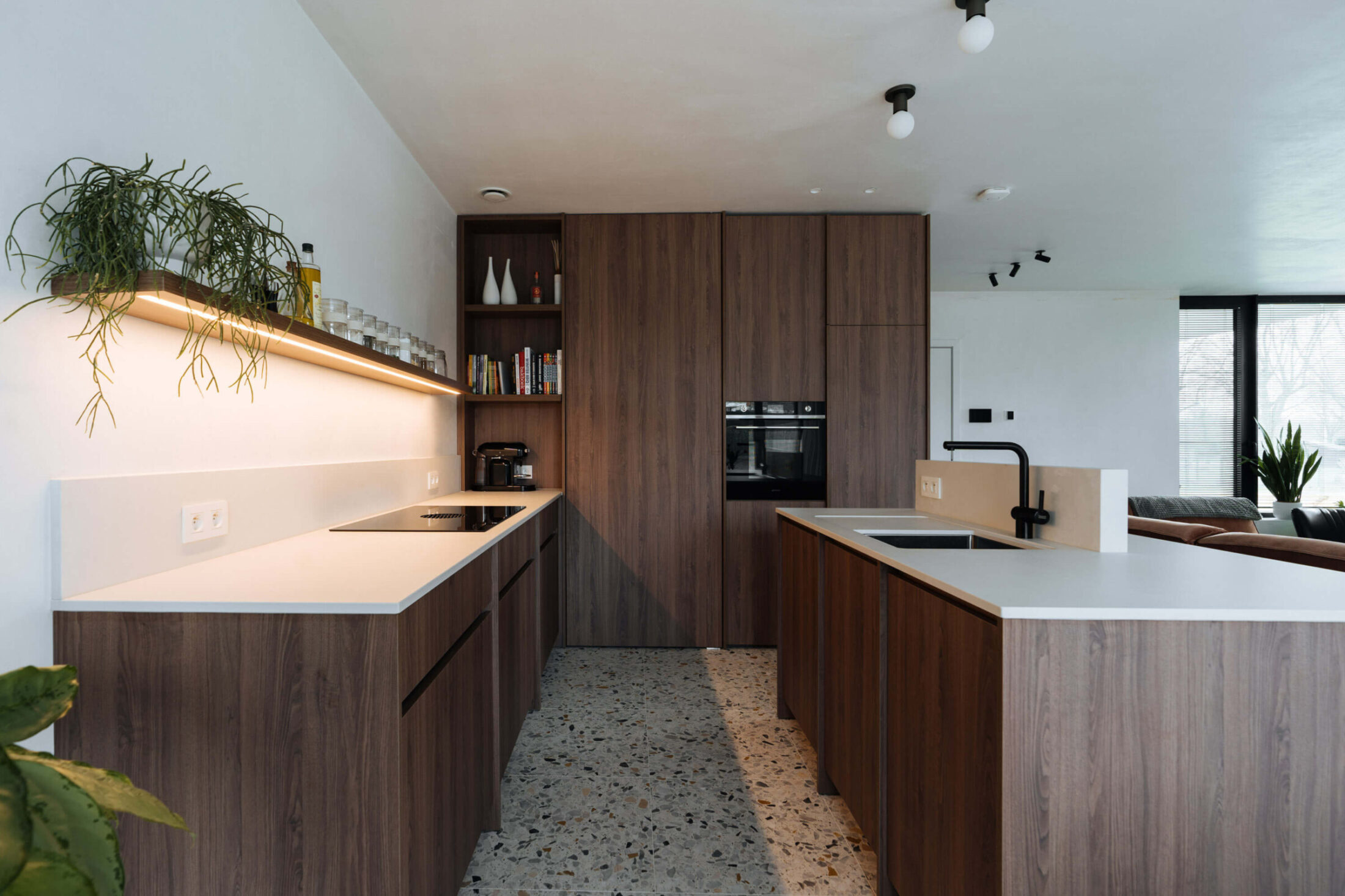 Moderne keuken met twee donkere houten blokken, wit werkblad en verlichte wandplank in Roeselare, Kaster Keukens