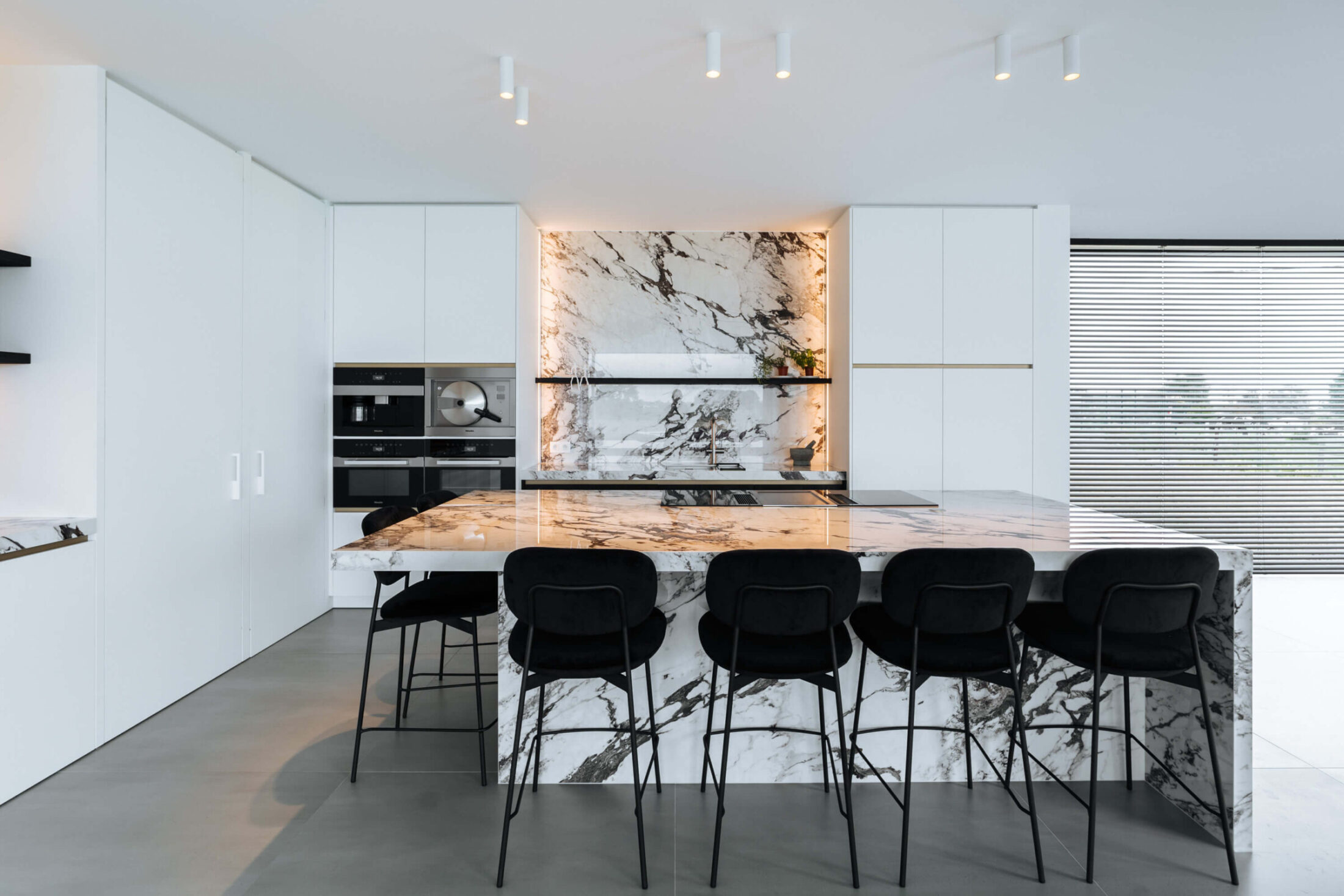 Moderne keuken met marmerlook eiland, zwarte barkrukken en witte kastenwand in Wevelgem, Kaster Keukens