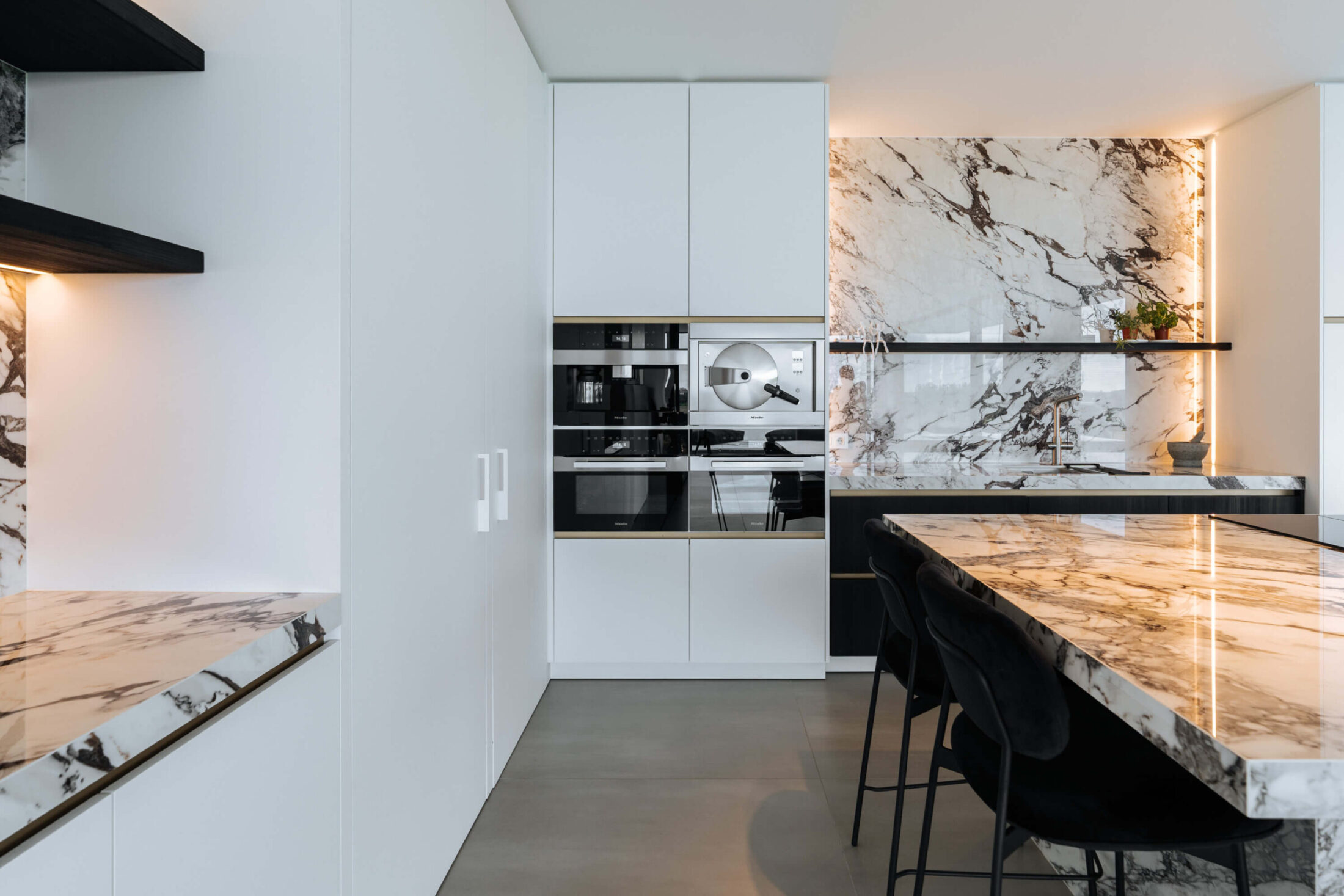 Moderne keuken met marmerlook achterwand, witte hoge kasten en ingebouwde ovens in Wevelgem, Kaster Keukens