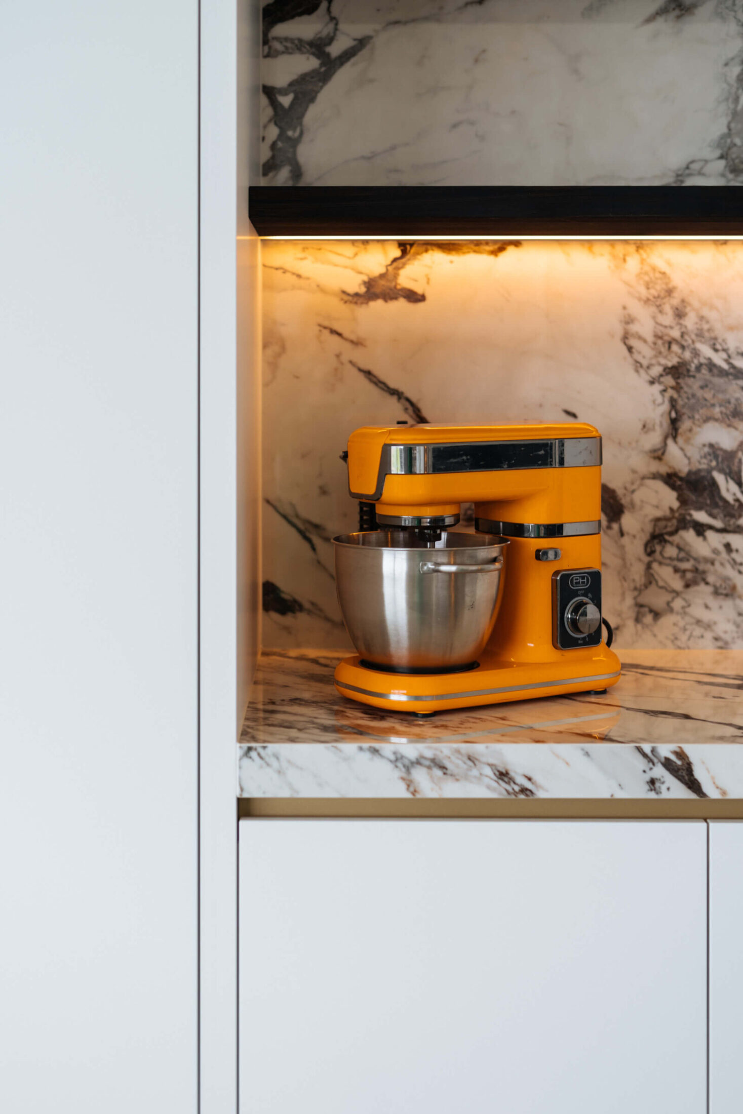 Detail van een moderne keuken met verlichte nis en marmerlook achterwand in Wevelgem, Kaster Keukens