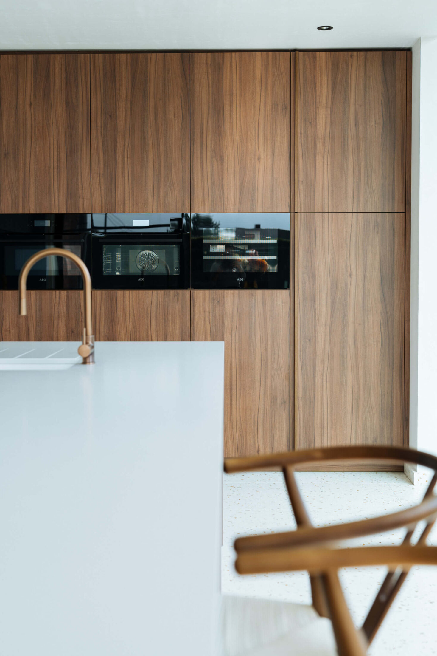 Detail van een scandinavische keuken met ovens in een notelaar kastenwand in Ardooie, Kaster Keukens