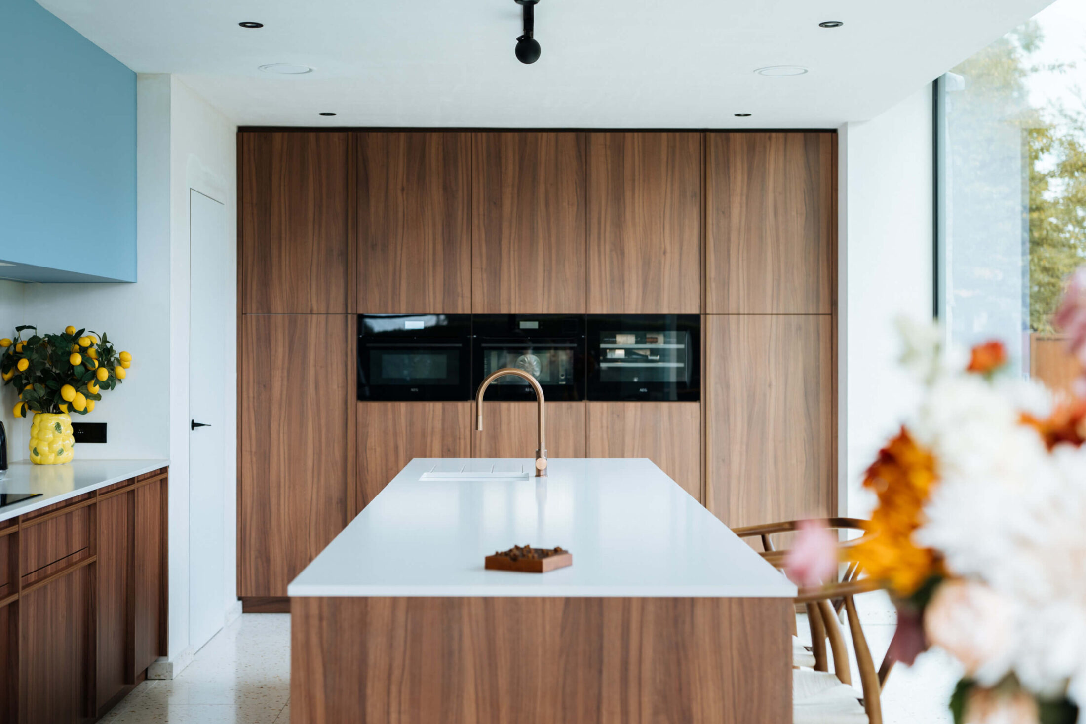 Scandinavische keuken met notelaar kastenwand, wit eiland en gouden kraan in Ardooie, Kaster Keukens