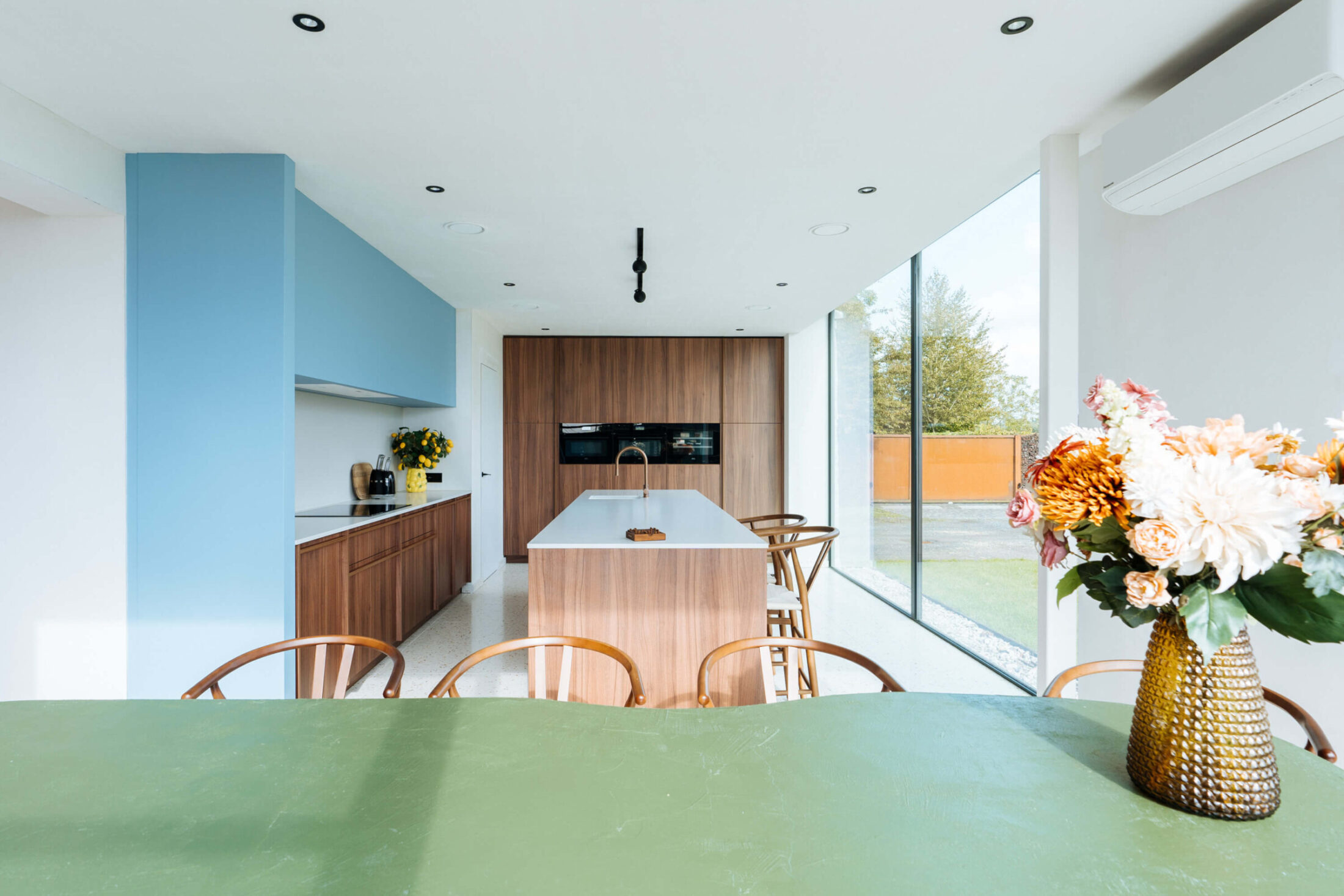 Scandinavische keuken met lichtblauwe kast, notelaar kastenwand en groene eettafel in Ardooie, Kaster Keukens