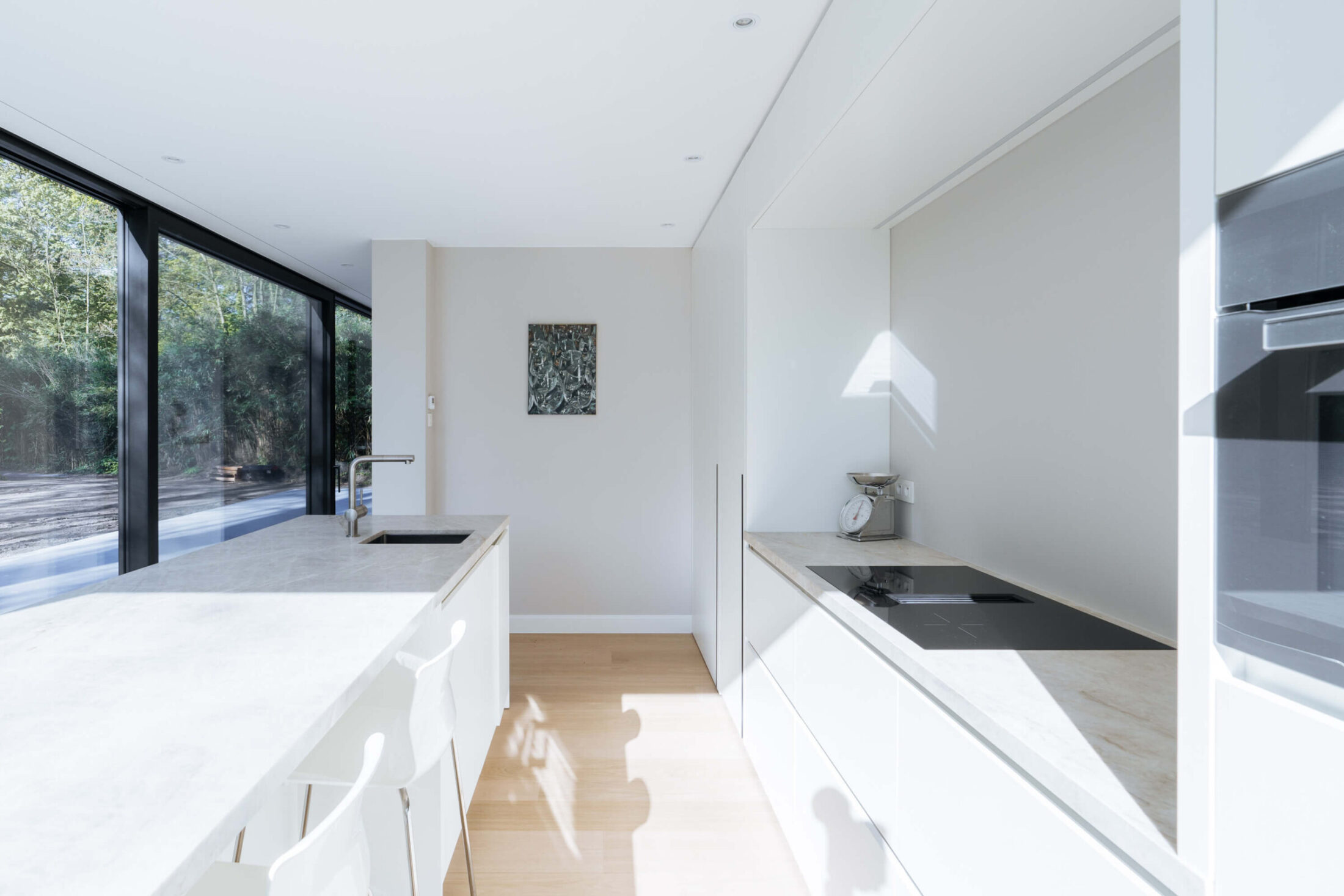 Scandinavische keuken met witte kasten, lang eiland en houten vloer in Brugge, Kaster Keukens