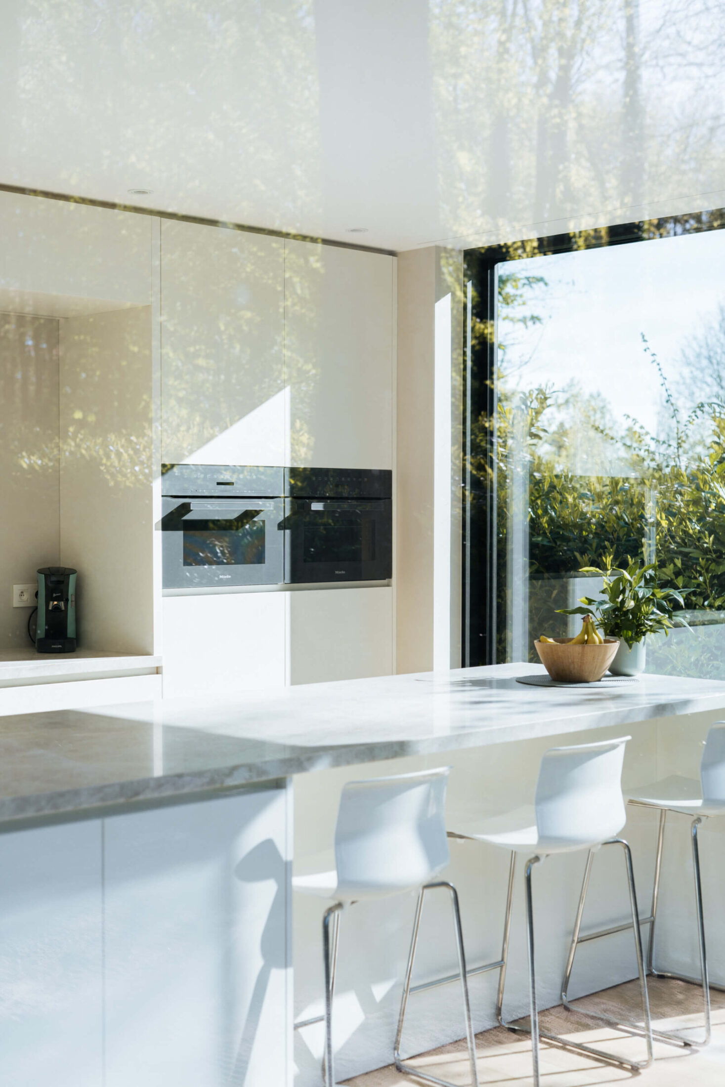 Scandinavische keuken met witte barkrukken aan een eiland met grijs werkblad in Brugge, Kaster Keukens