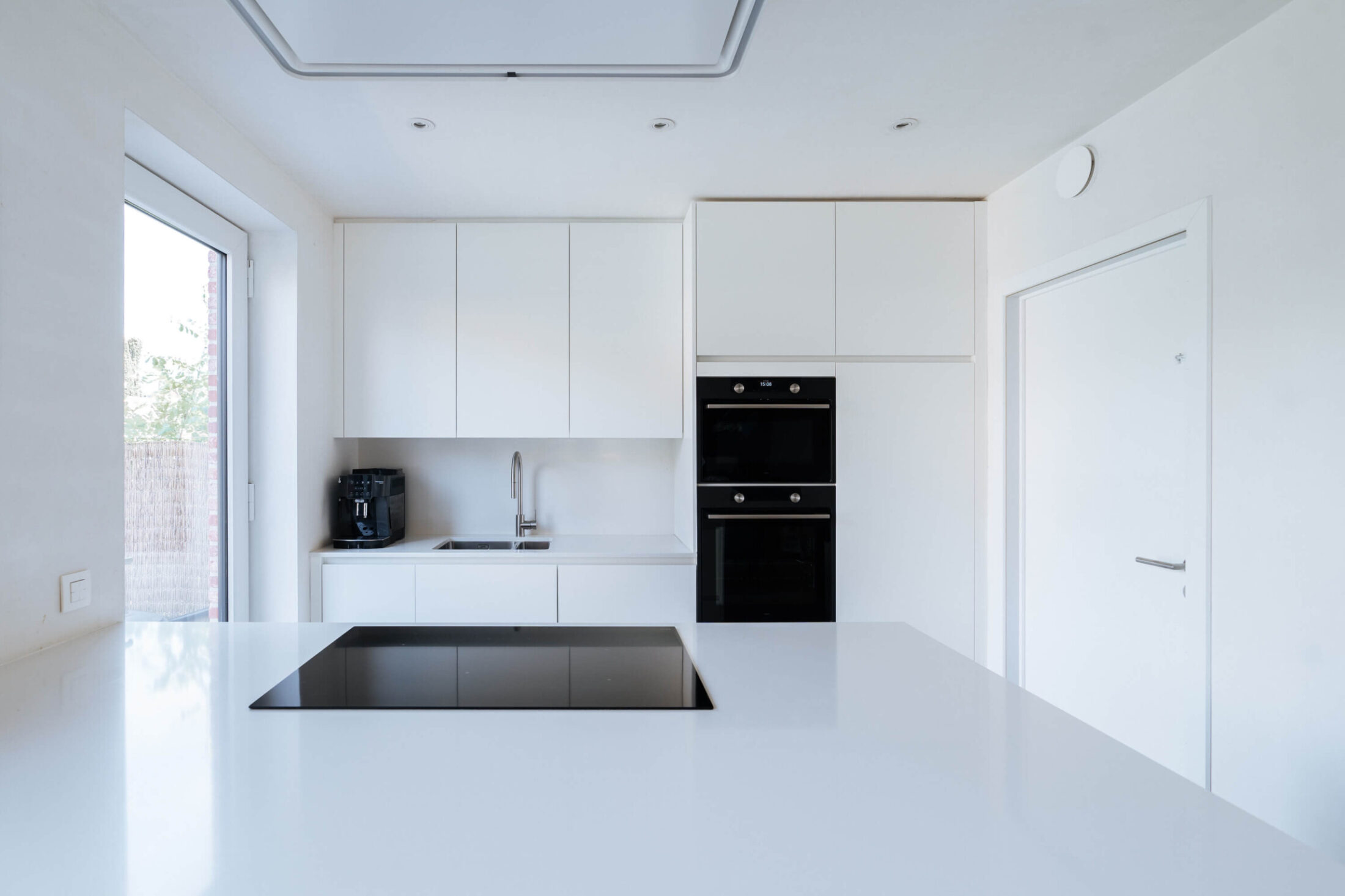 Scandinavische keuken met wit kookeiland, inductiekookplaat en hoge kasten in Brugge, Kaster Keukens