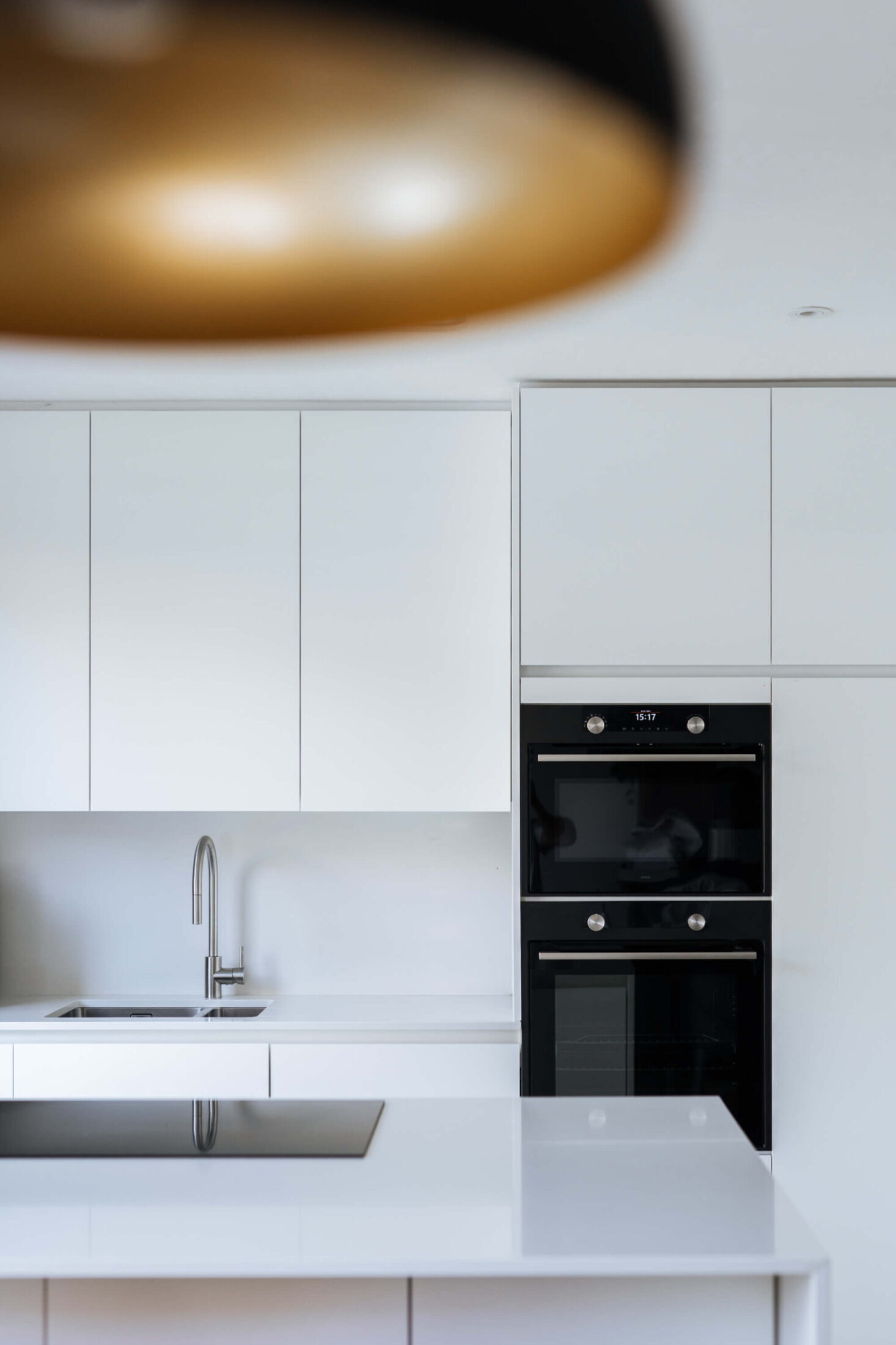 Scandinavische keuken met witte fronten, zwarte ovens en koperen hanglamp in Brugge, Kaster Keukens