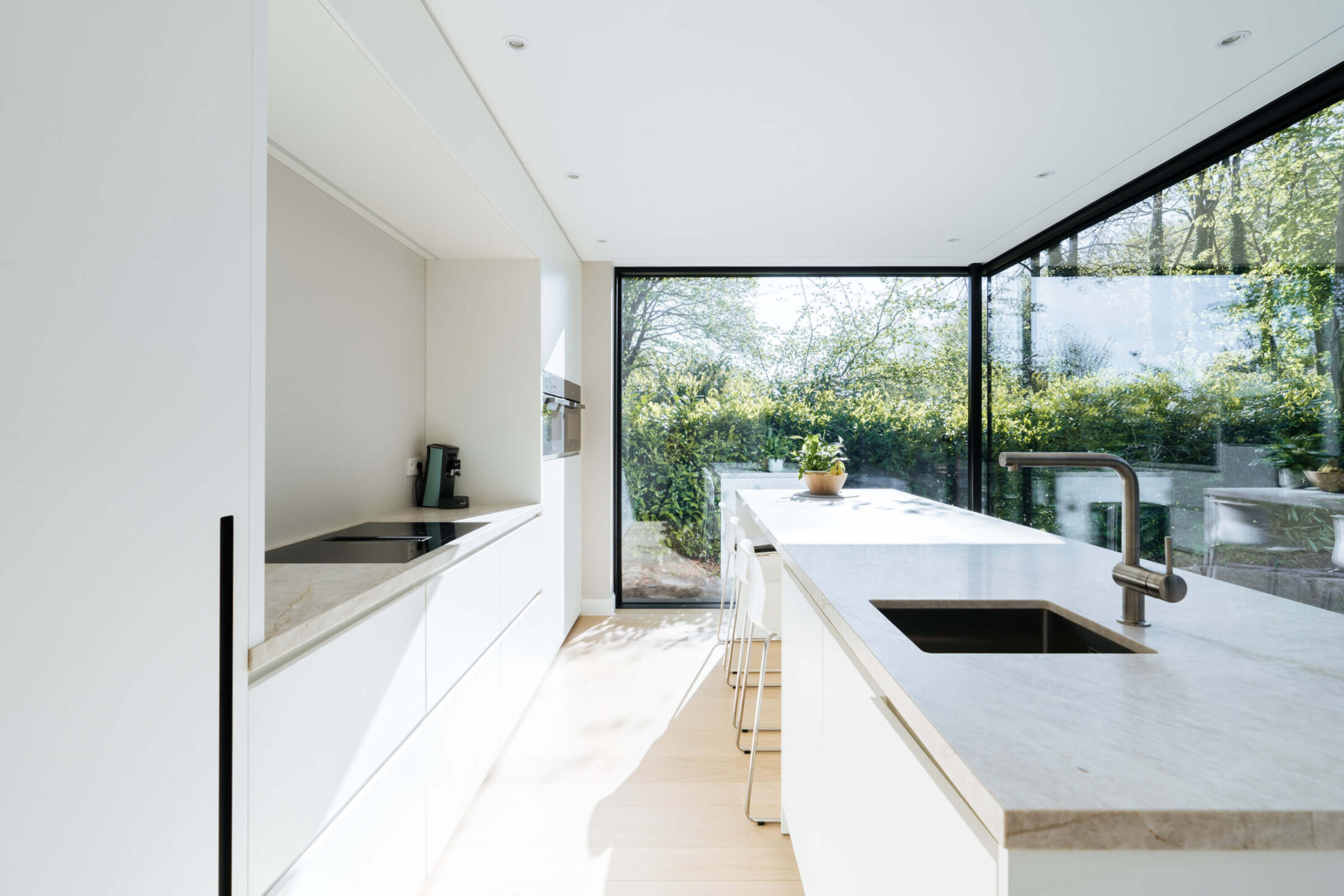 Scandinavische keuken met witte fronten, licht natuurstenen werkblad en tuinzicht in Brugge, Kaster Keukens