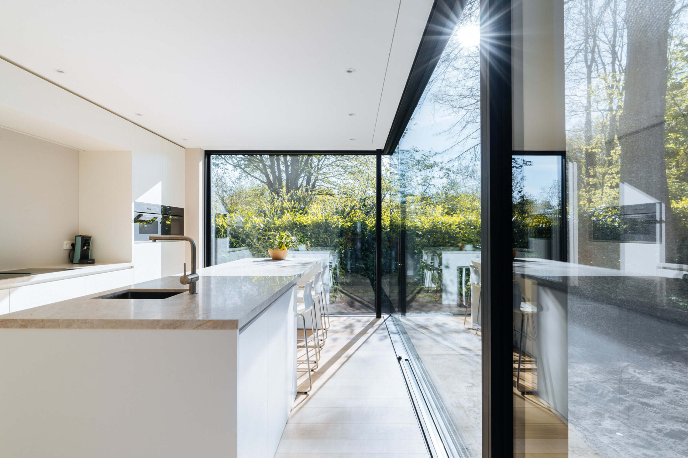 Scandinavische keuken met wit eiland en glazen hoekraam naar de tuin in Brugge, Kaster Keukens