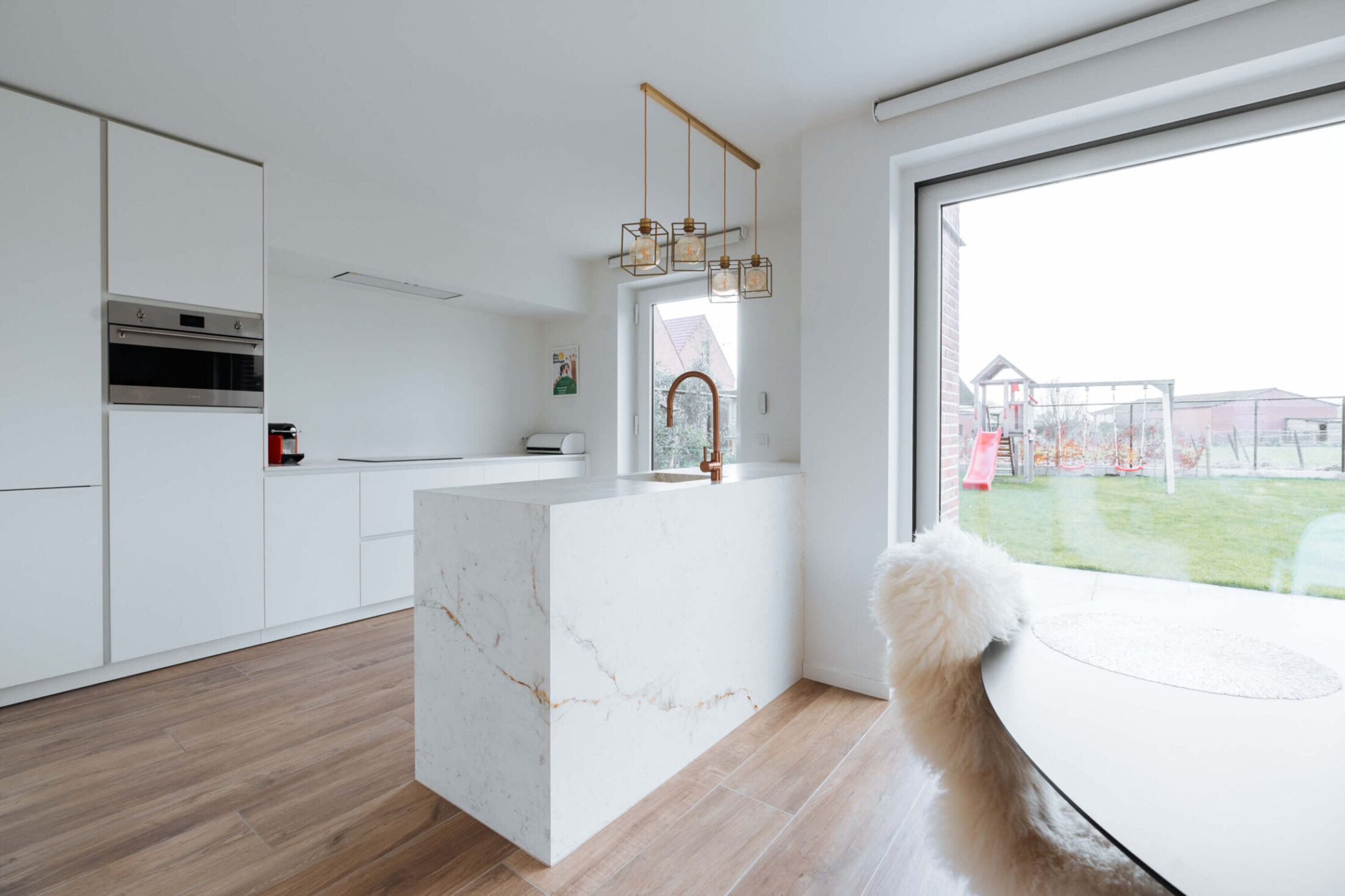 Scandinavische keuken met marmerlook kookeiland, witte kasten en koperen hanglampen in Herzele, Kaster Keukens