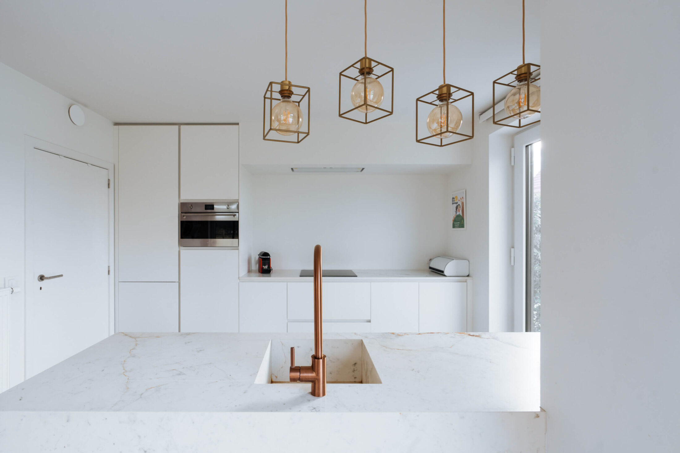 Scandinavische keuken met marmerlook eiland, koperen kraan en witte hoge kasten in Herzele, Kaster Keukens