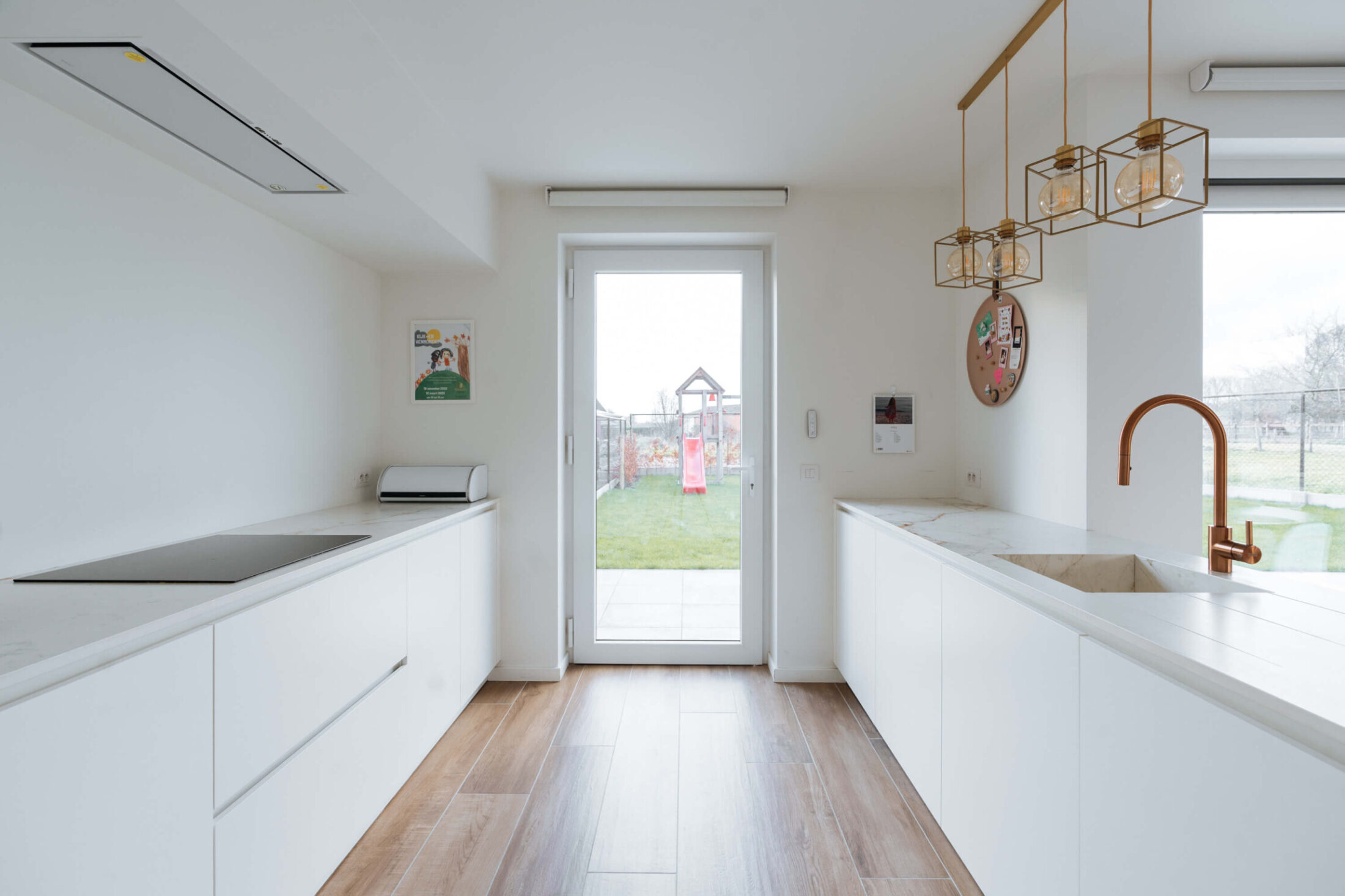 Scandinavische keuken met witte werkbanken, koperen kraan en tuindeur in Herzele, Kaster Keukens