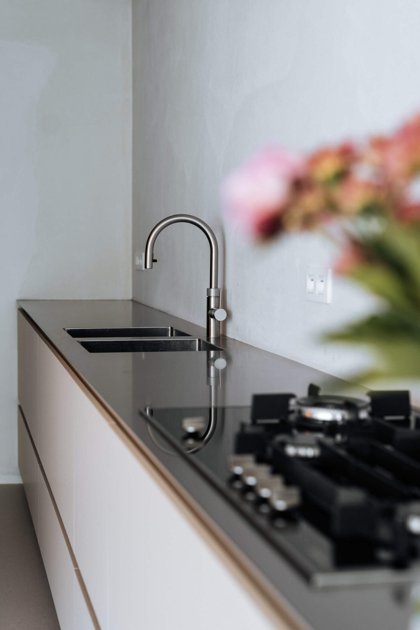 Detail van een Scandinavische keuken met donker werkblad, gaskookplaat en inox kraan in Lauwe, Kaster Keukens
