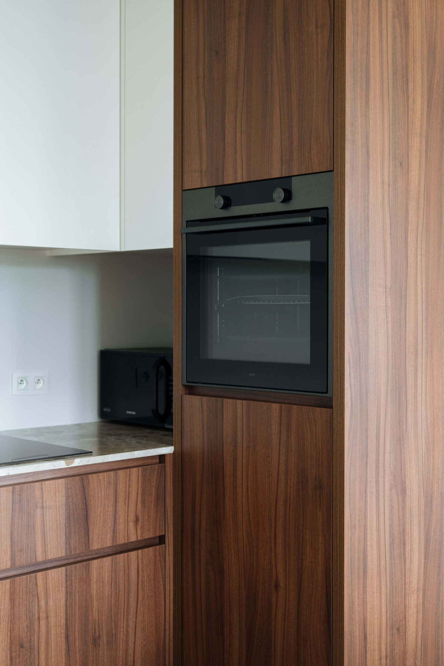 Detail van een Scandinavische keuken met notelaren hoge kast en ingebouwde oven in Oostende, Kaster Keukens