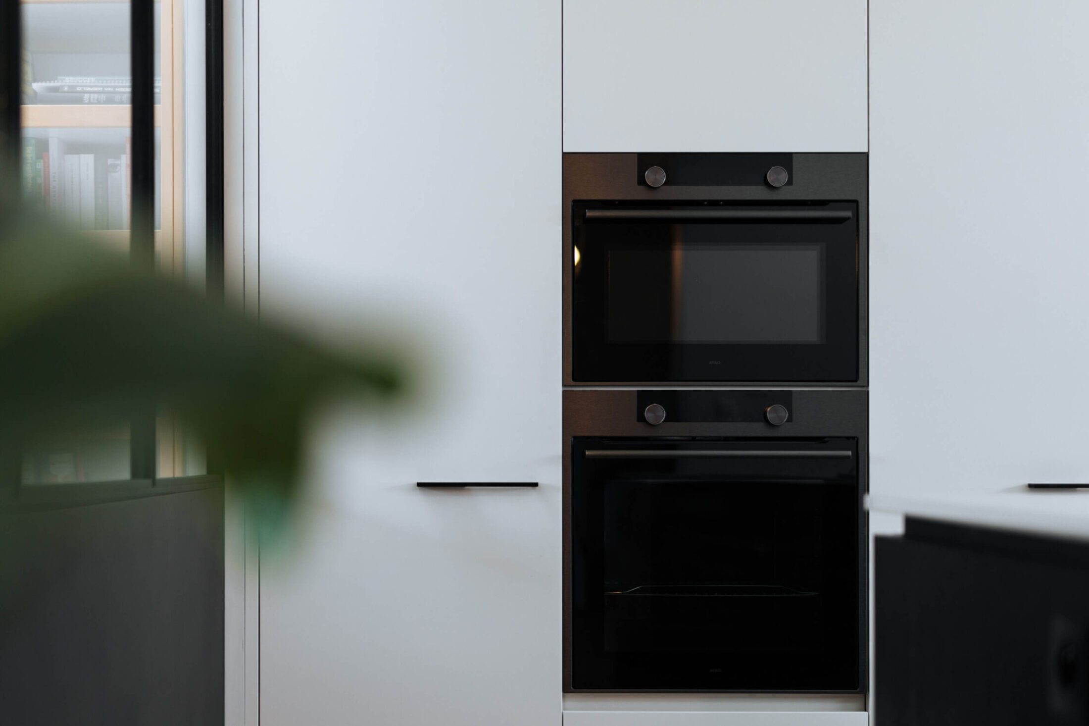 Scandinavische keuken met witte hoge kasten en twee zwarte ovens in Roeselare, Kaster Keukens