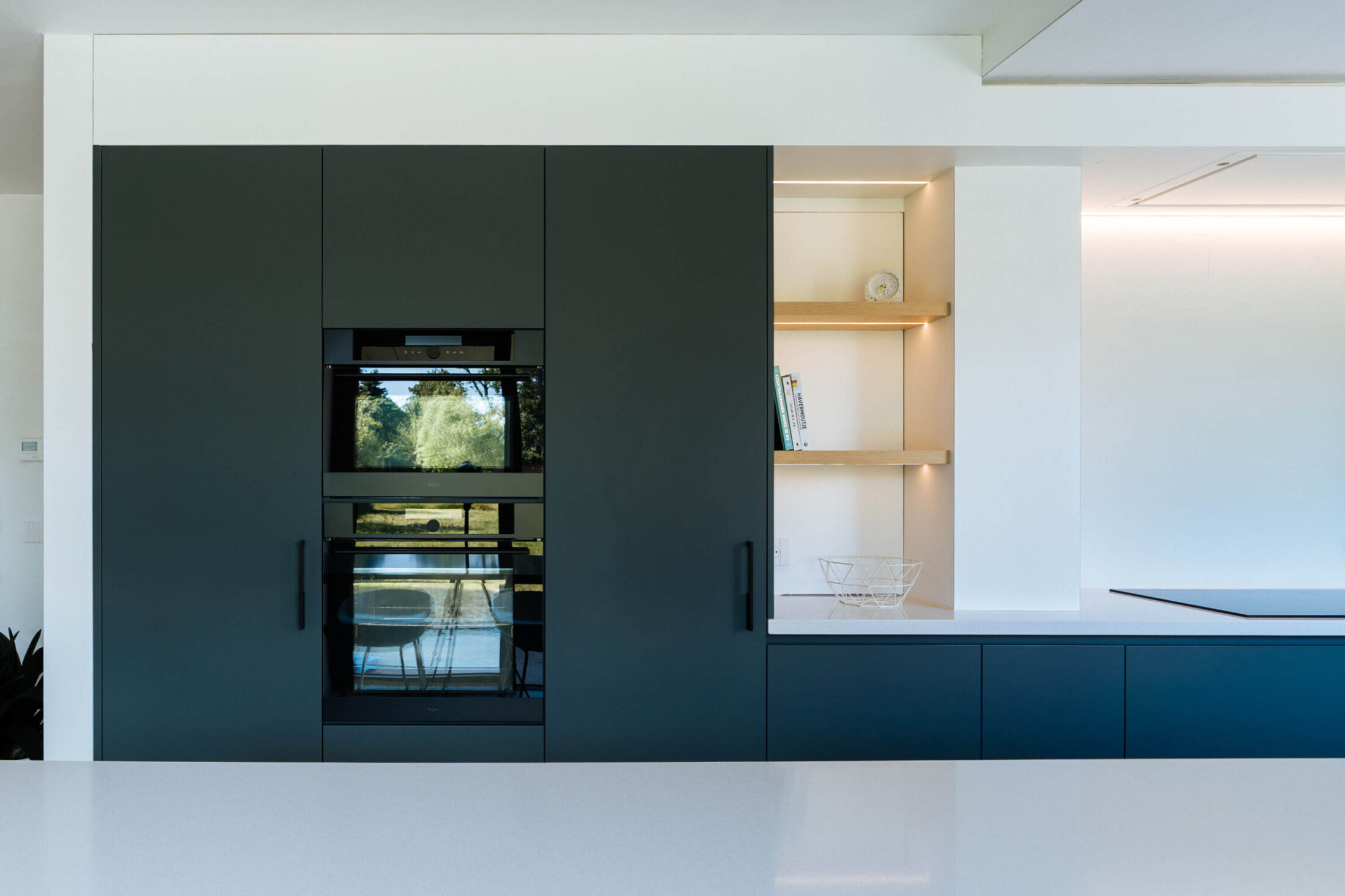 Scandinavische keuken met donkerblauwe kastenwand, twee ovens en eiken nissen in Roeselare, Kaster Keukens
