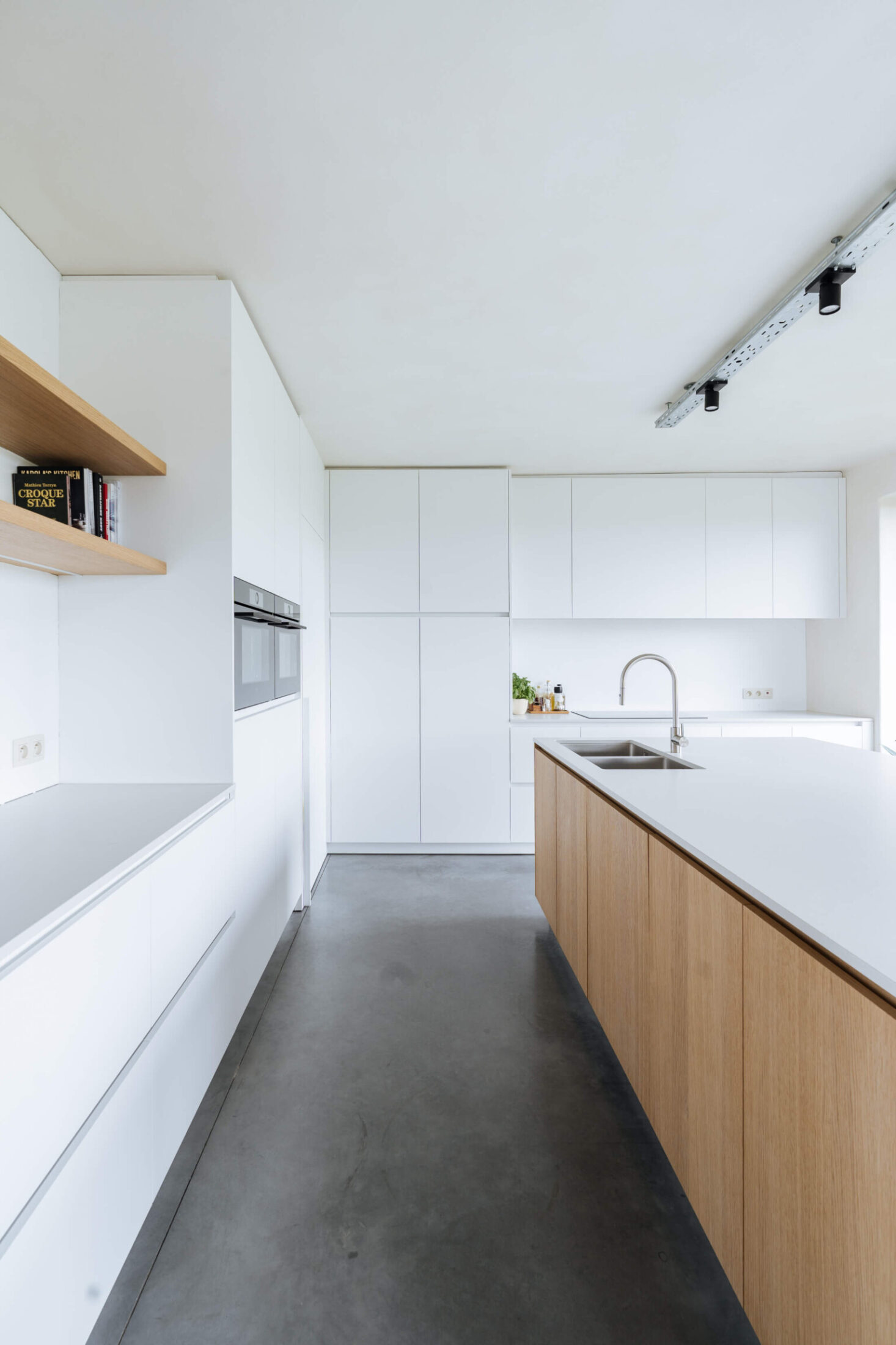 Scandinavische keuken met witte kasten, eiken eiland en betonvloer in Wevelgem, Kaster Keukens
