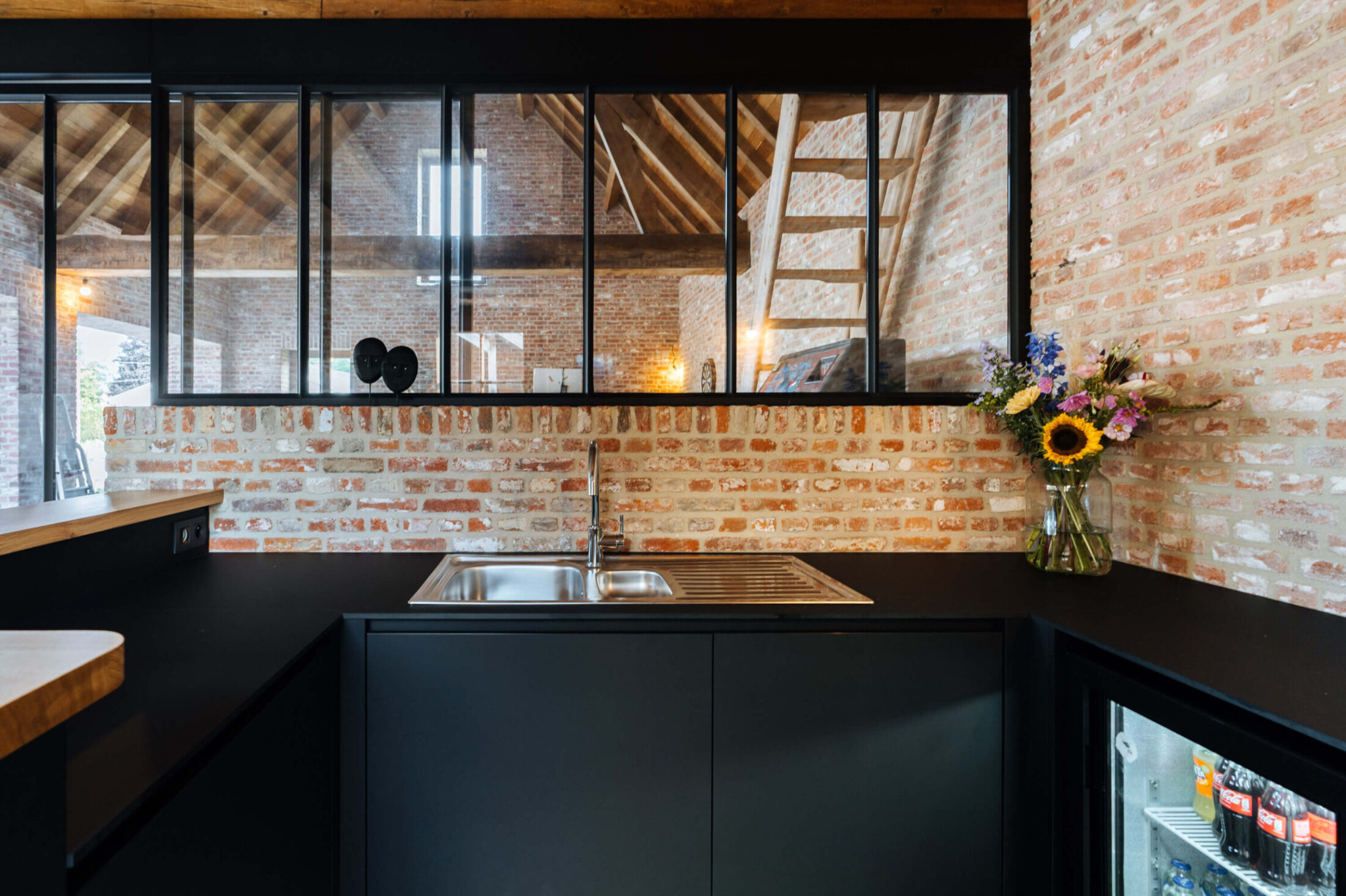Bar op maat met zwarte kasten, inox spoelbak en glazen binnenwand in Beveren, Kaster Keukens